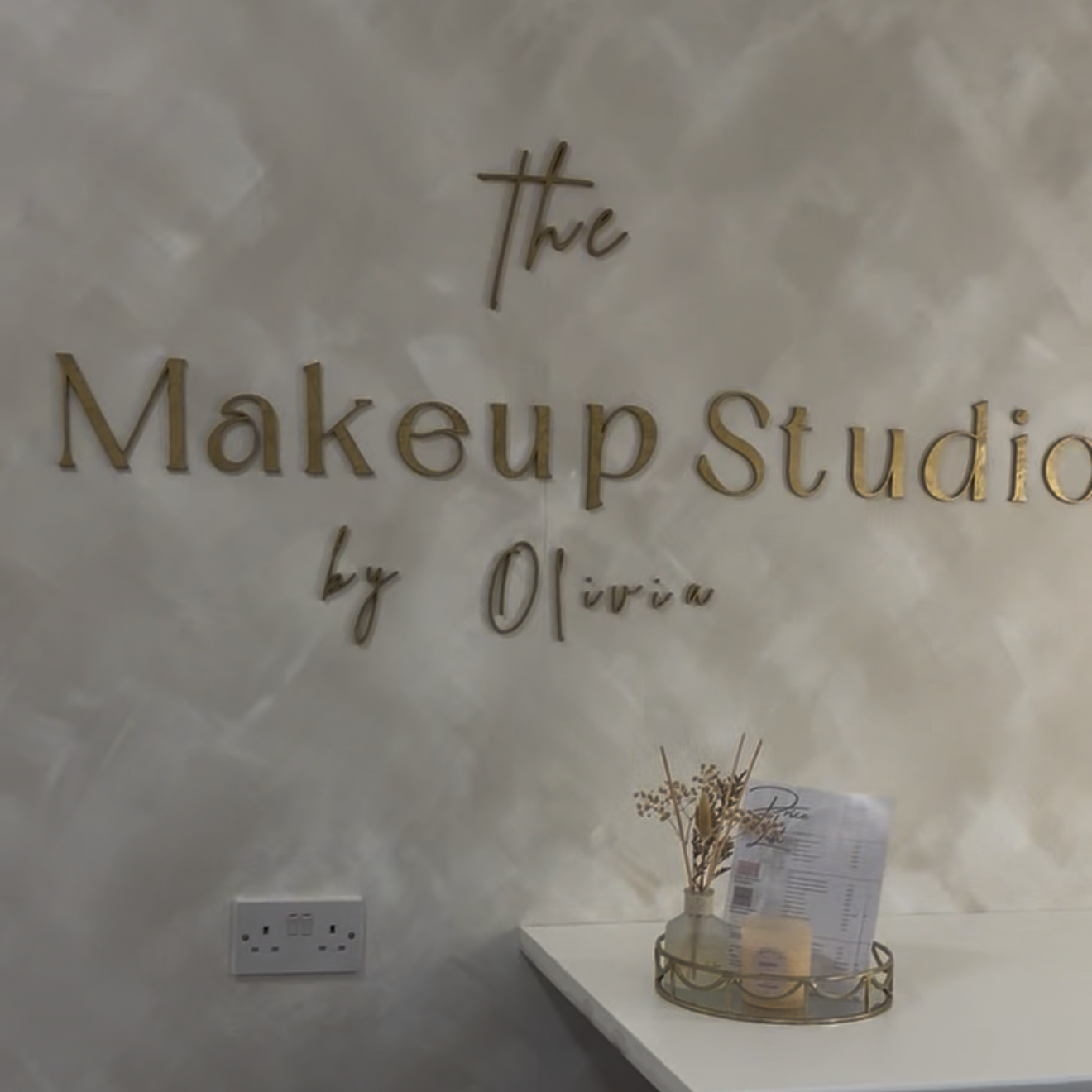 Sign for The Makeup Studio by Olivia, with a small table holding decorative plants and a menu or flyer on a stand.