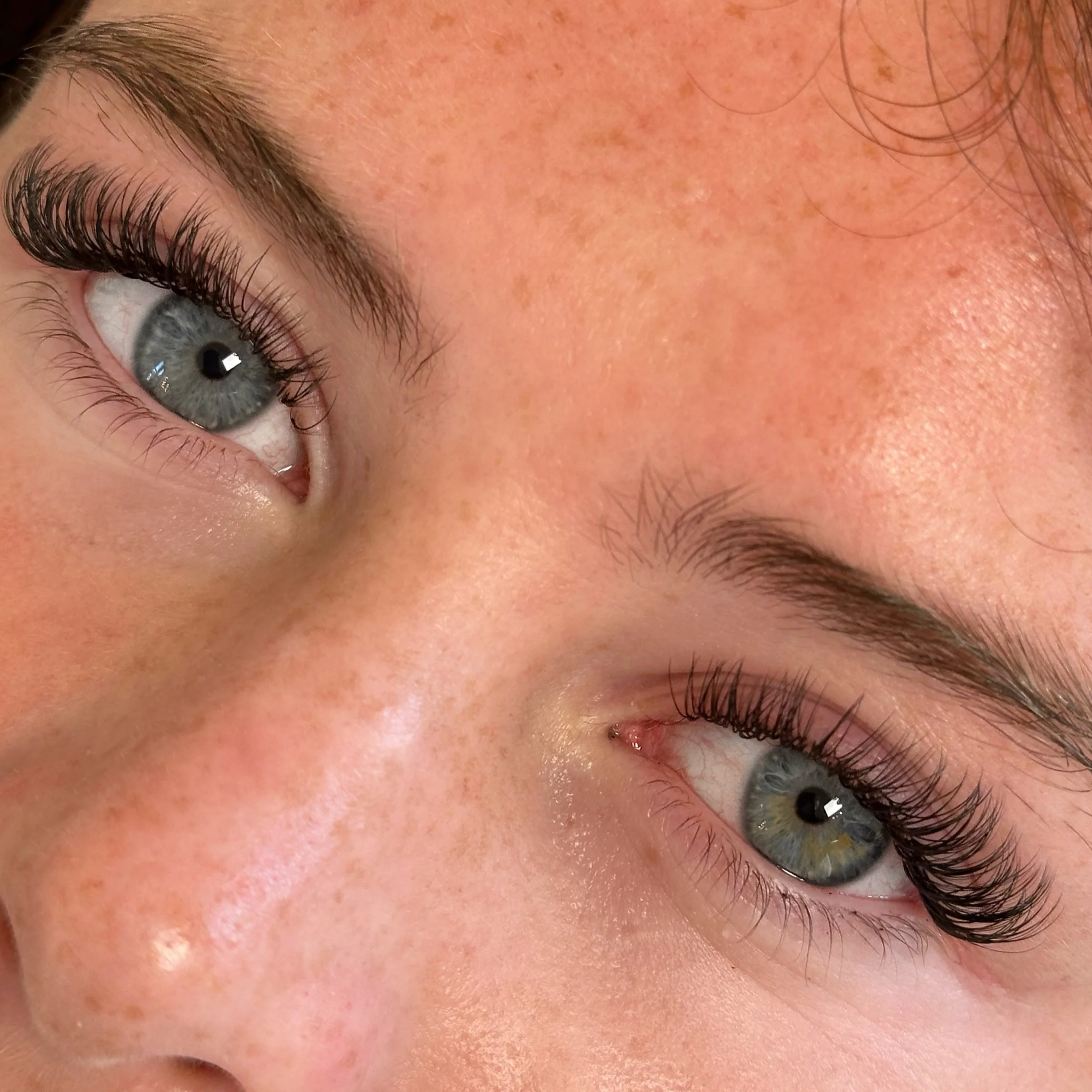 Close-up of a person's eye and part of their face, showing blue eye color, long eyelashes, and freckles on the skin.