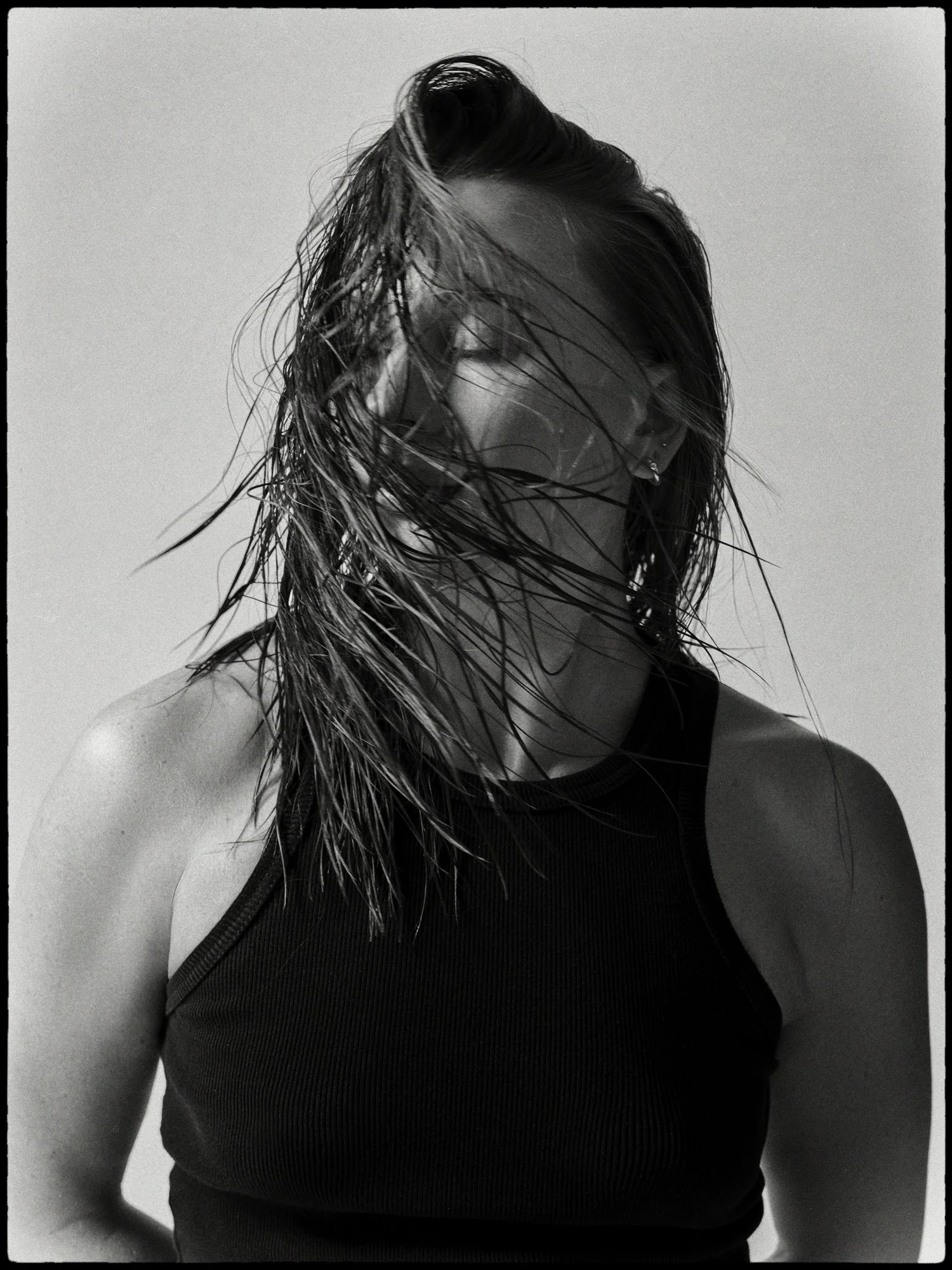 Black and white photo of a woman with wet hair wearing a sleeveless top, looking down with her face slightly obscured by her hair.
