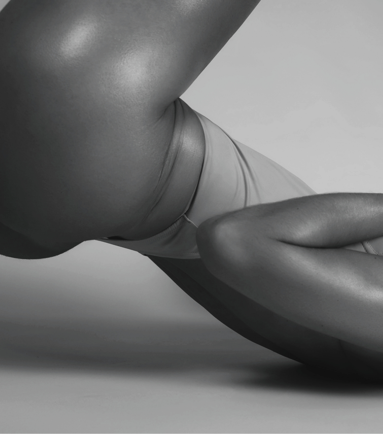 Close-up black-and-white photograph of a person performing a yoga pose on the floor, wearing a fitted shirt and shorts.