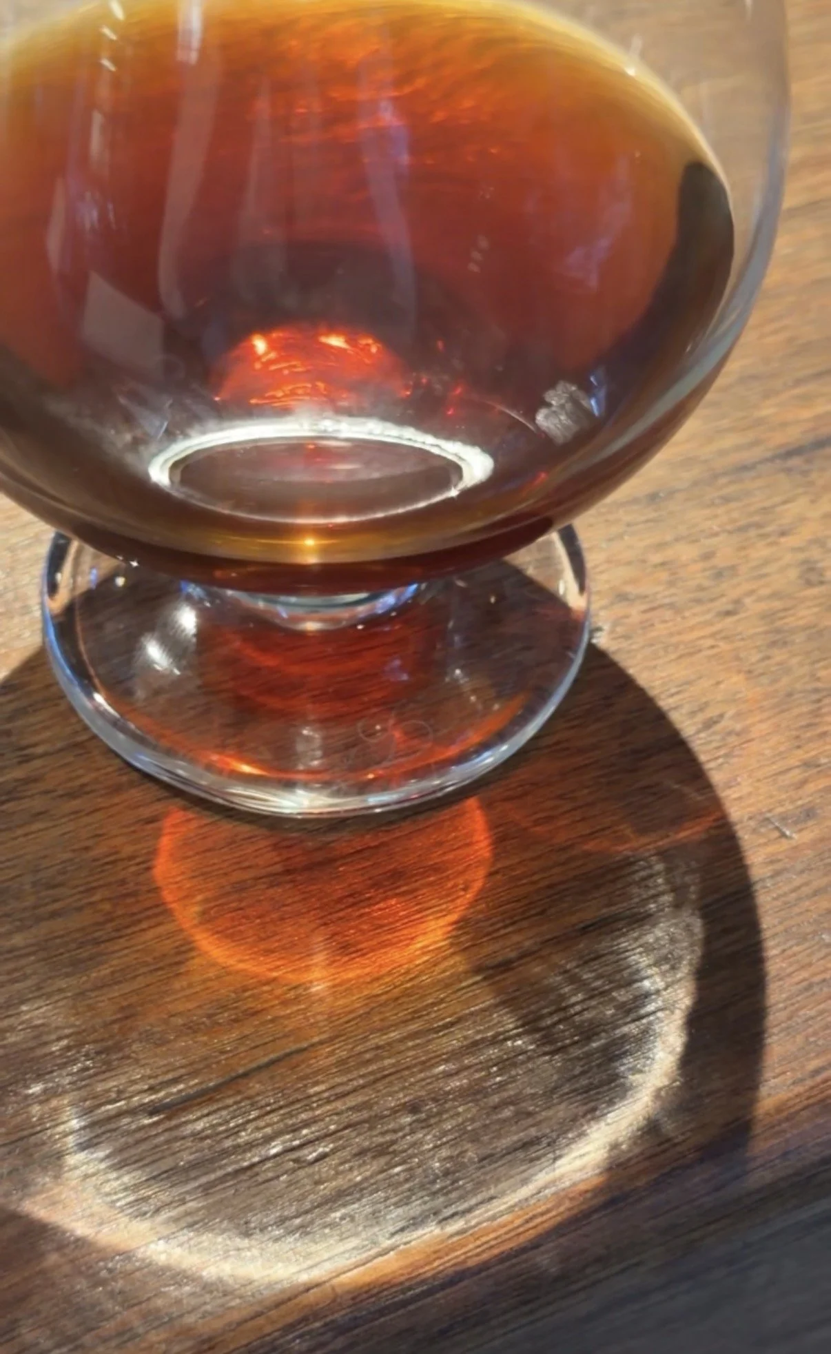 A glass of coffee on a wooden table with sunlight casting a reflection and shadow.
Image by Yineth Garcia