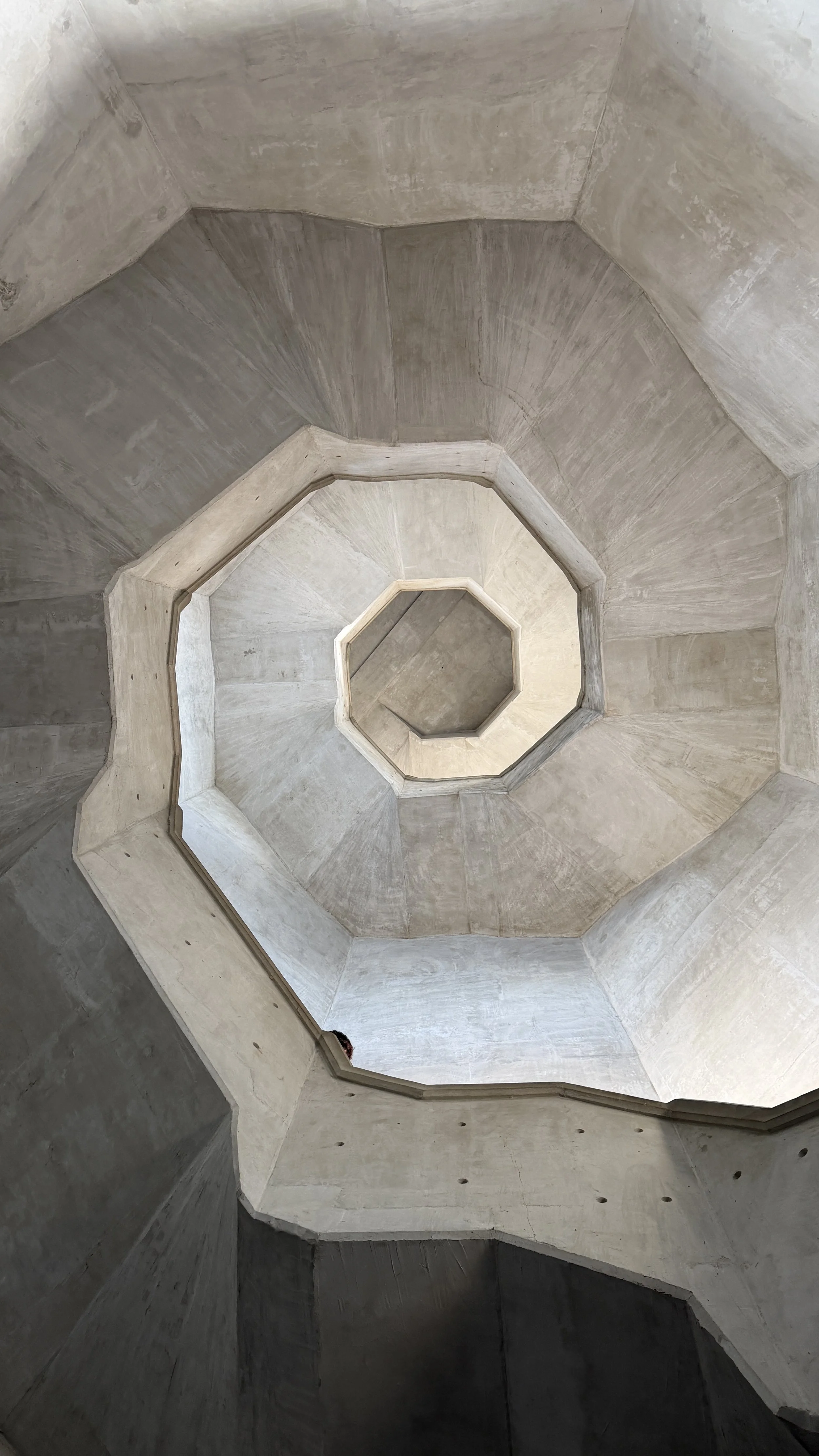 Looking up from the bottom of a multi-level concrete staircase with octagonal shape.