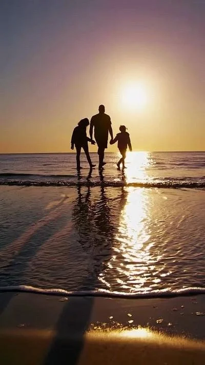 Silhouette of a family holding hands and walking in shallow water on the beach during sunset.