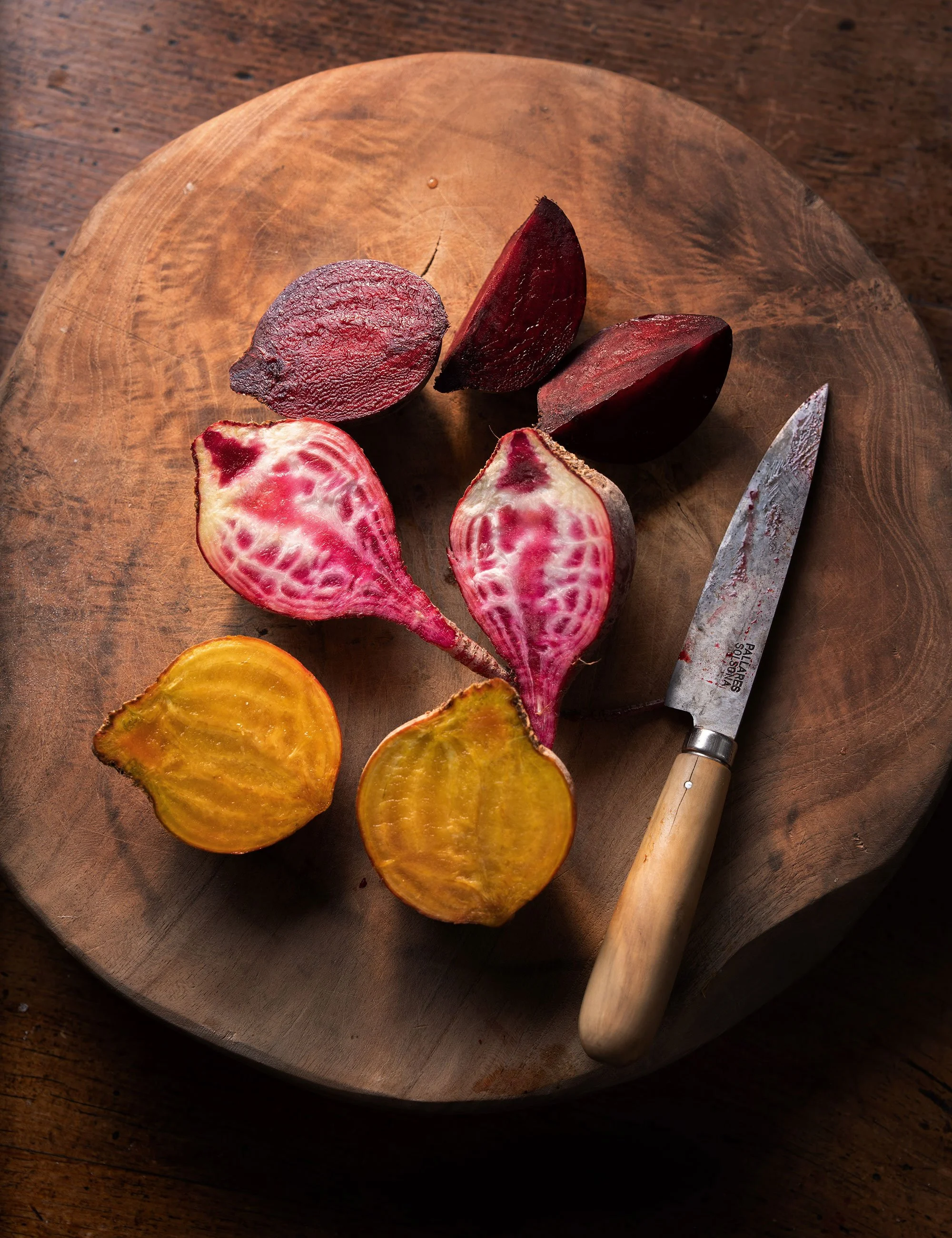 Colorful beets and knife on a wooden board in a rustic ingredient photograph.