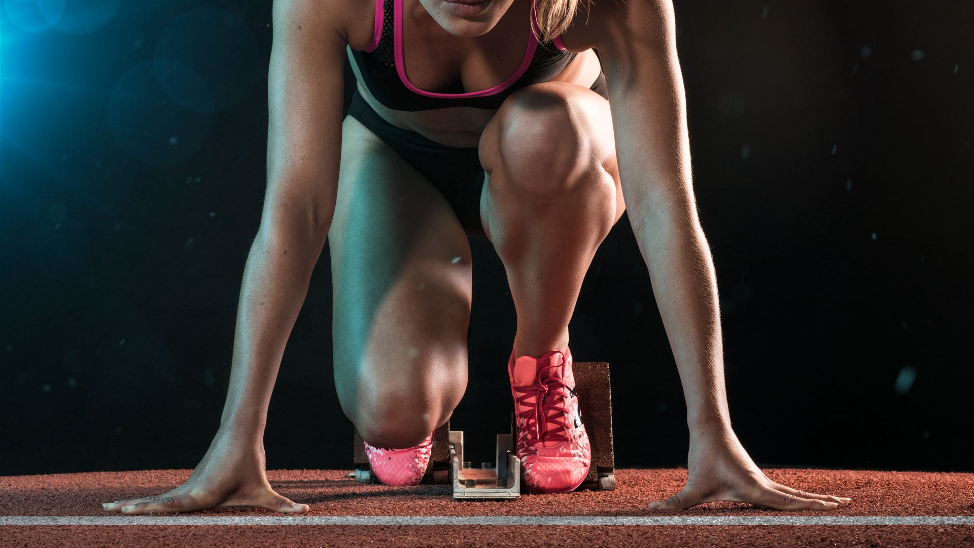 Runner poised at the starting line on a track, photographed in dramatic athletic campaign lighting.