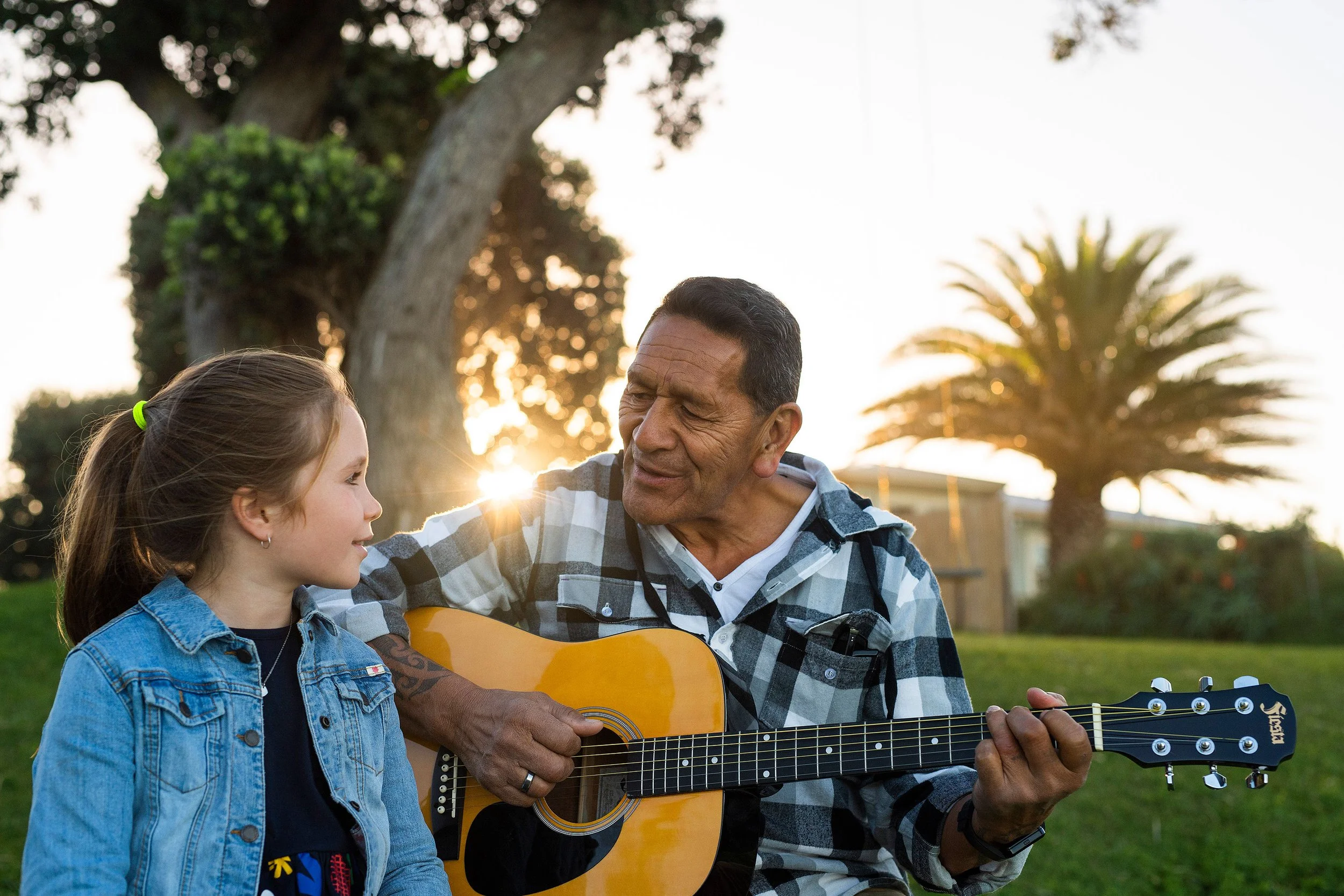 Father playing guitar for a child in a sunny outdoor family lifestyle portrait.
