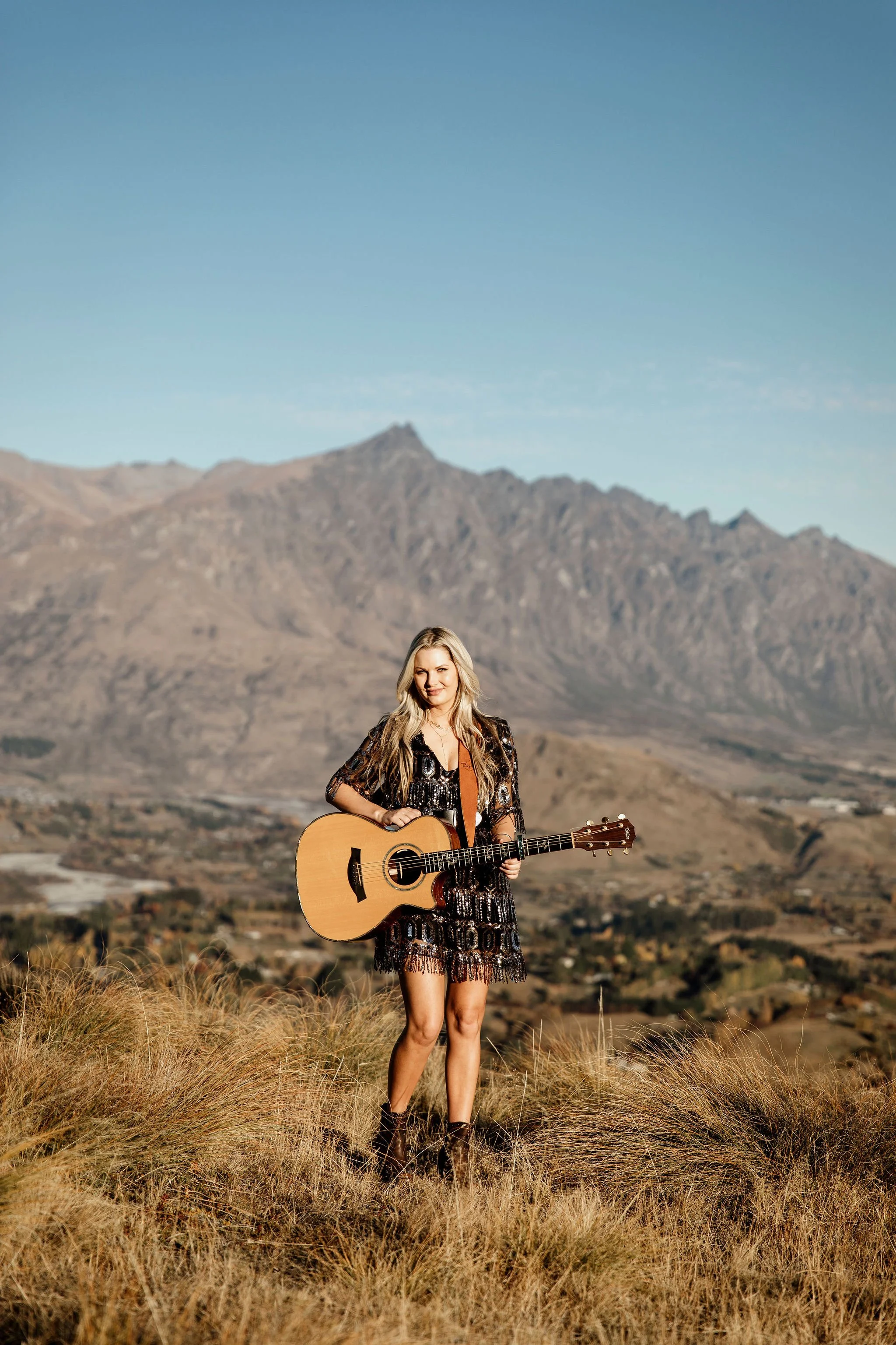 Musician Miranda holding a guitar in a dry open landscape with mountains behind her.