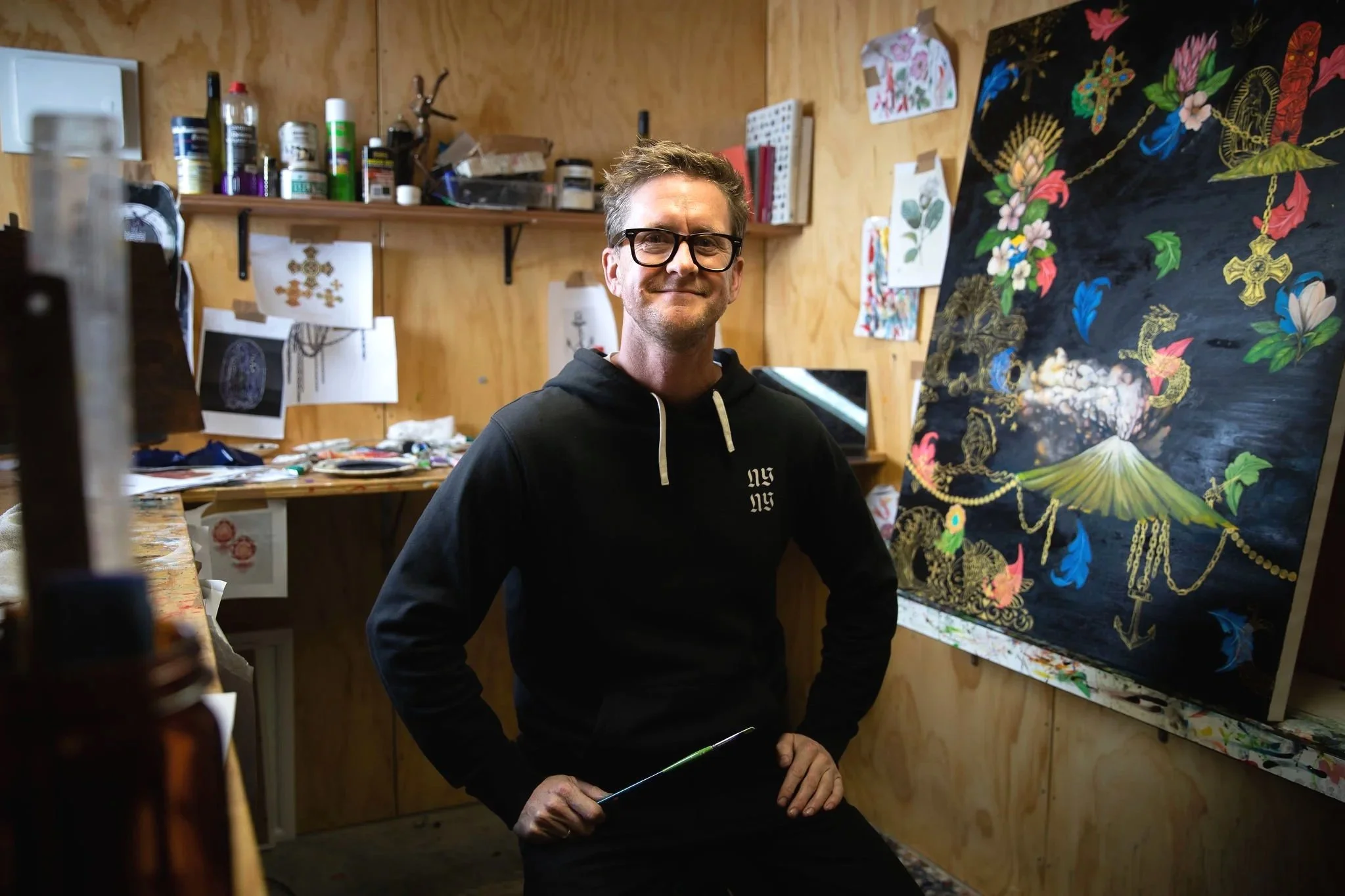 Artist Simon Morrison-Deaker standing in a colorful studio workspace.