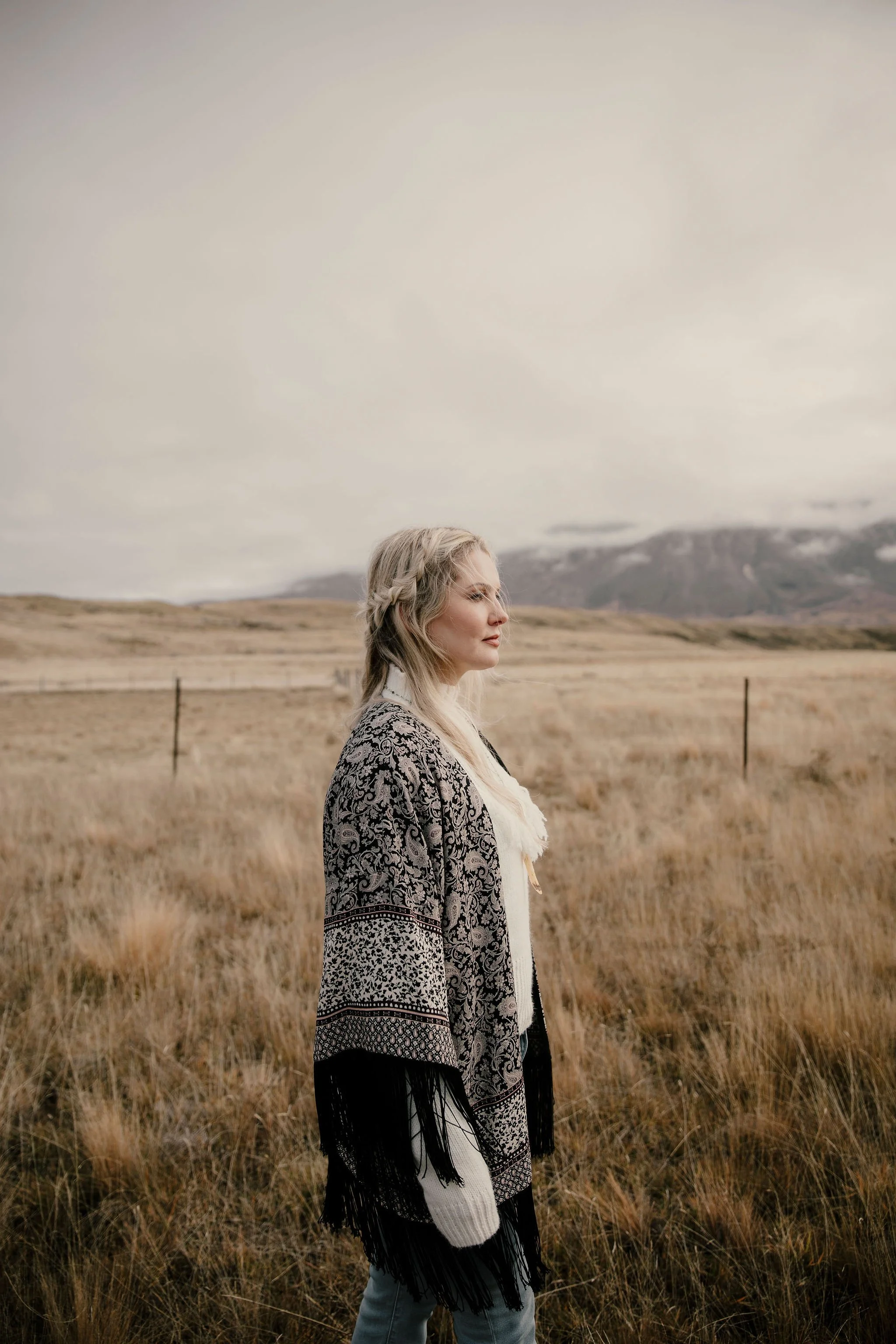 Artist portrait of a woman standing in a windswept field with soft muted landscape tones.