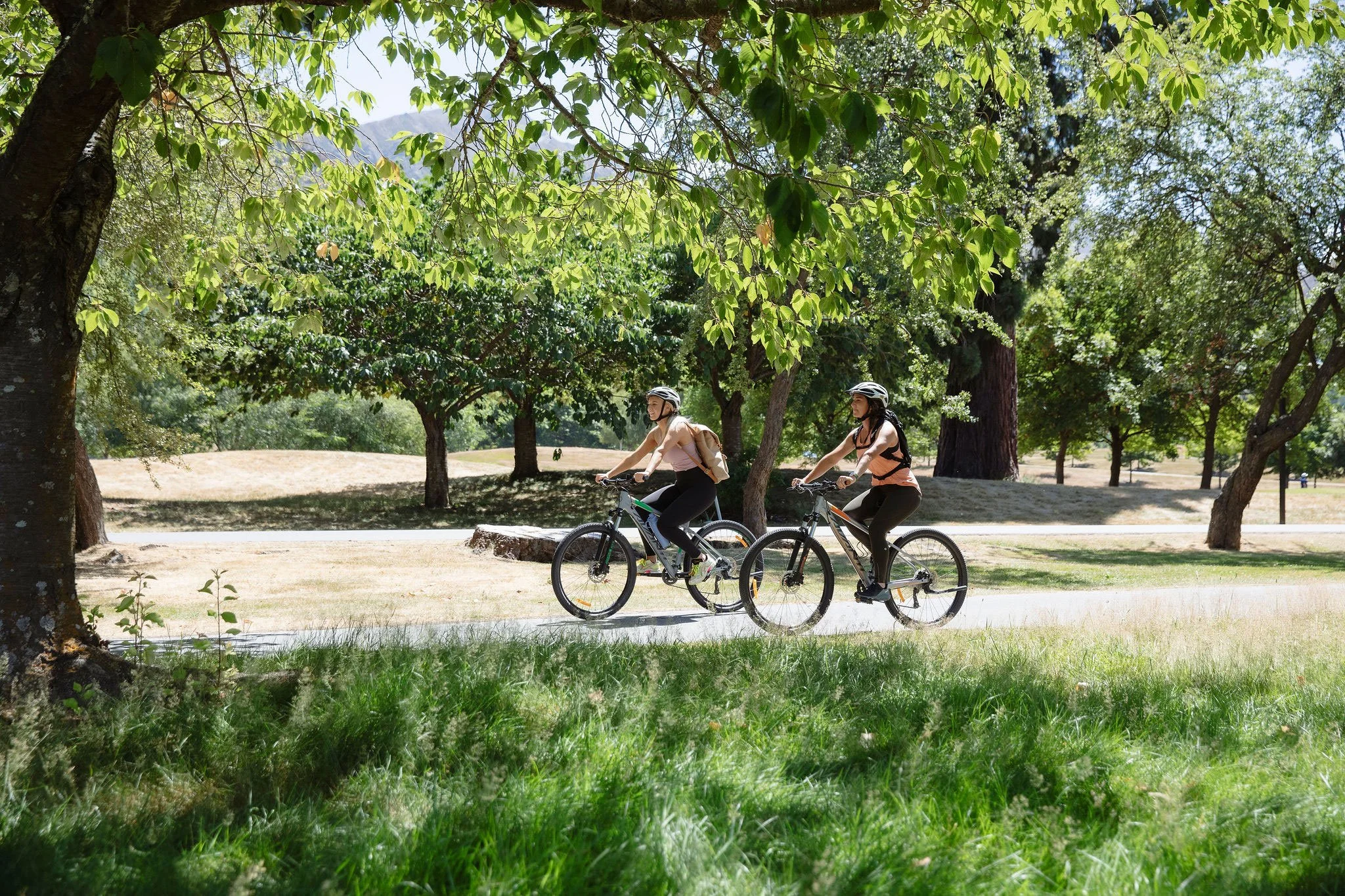 Guests cycling through landscaped resort grounds on a sunny Queenstown tourism shoot.