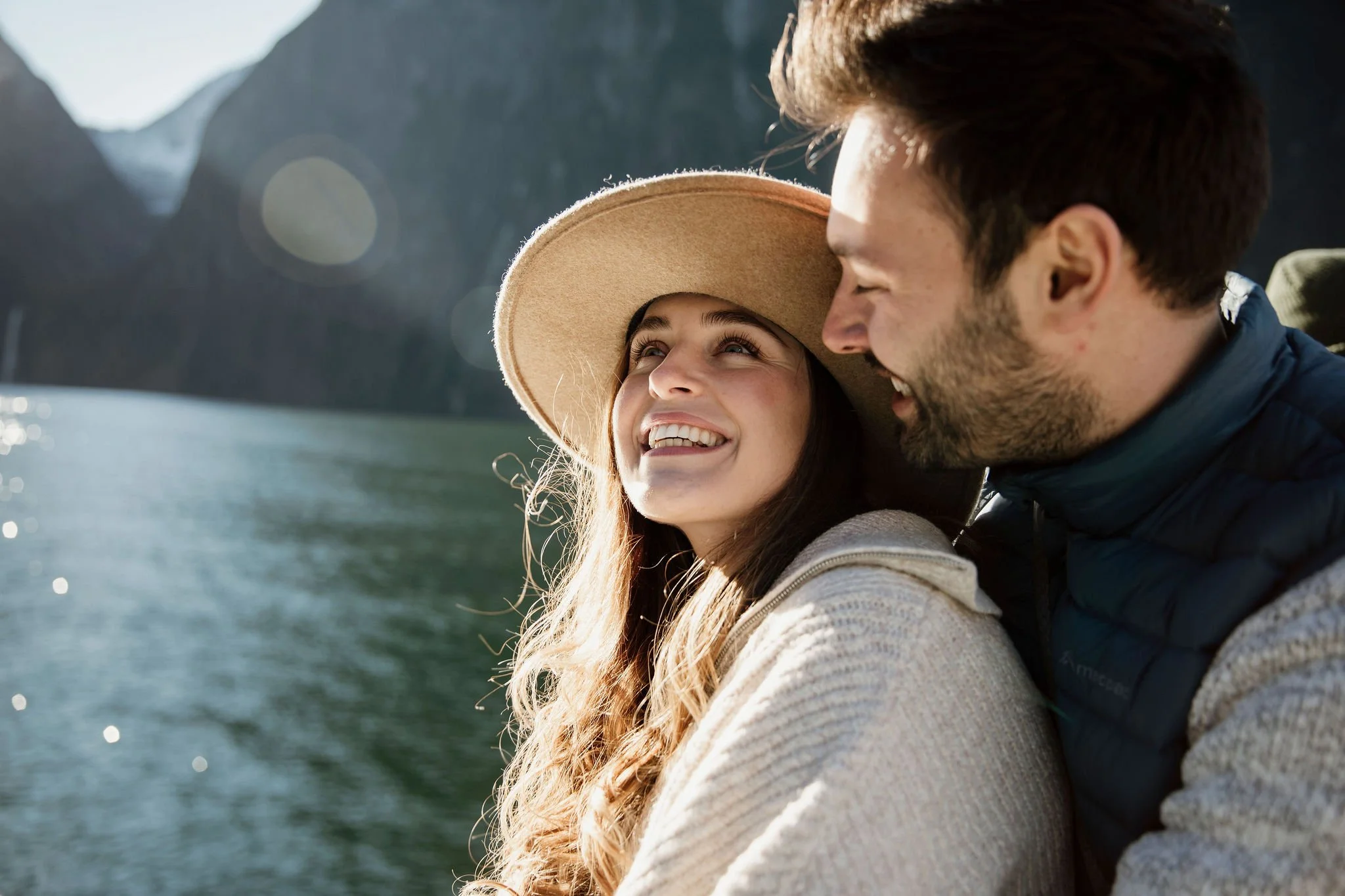 Couple smiling together on a scenic Milford Sound boat cruise with mountains and water behind them.