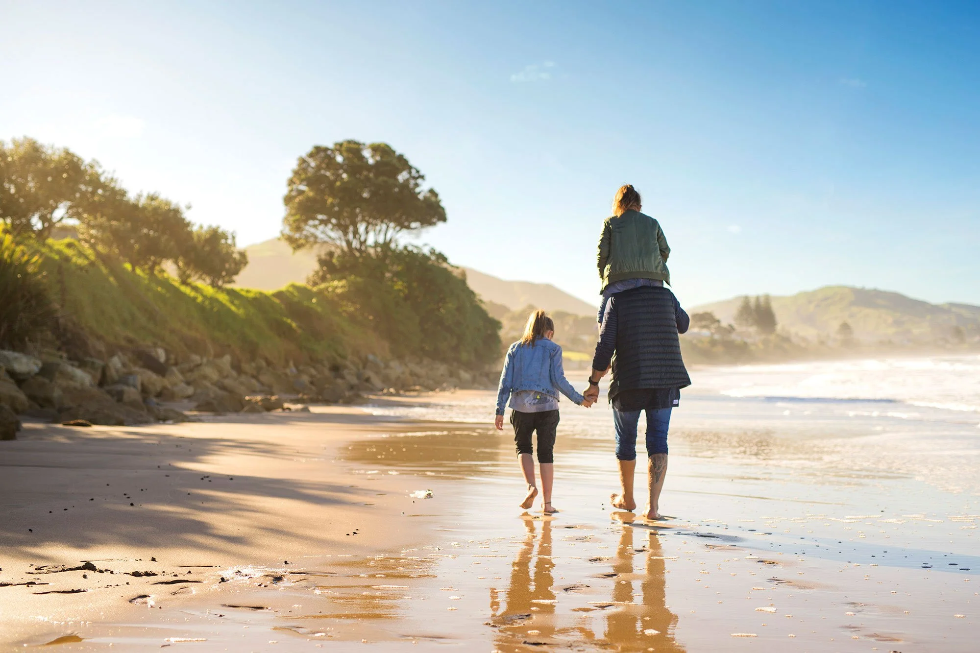 Adult and child walking hand in hand along a beach at low tide.