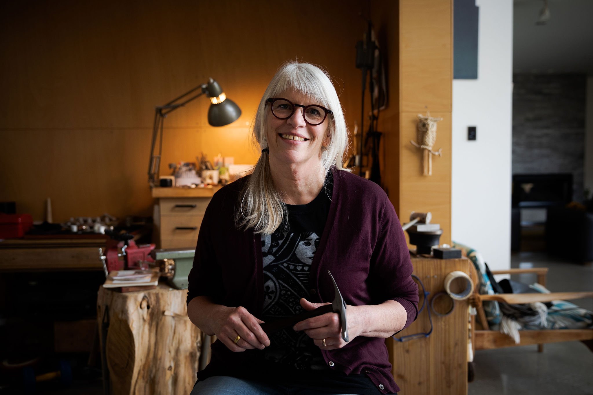 Artist Kay Turner smiling in a warm workshop setting with tools and materials behind her.