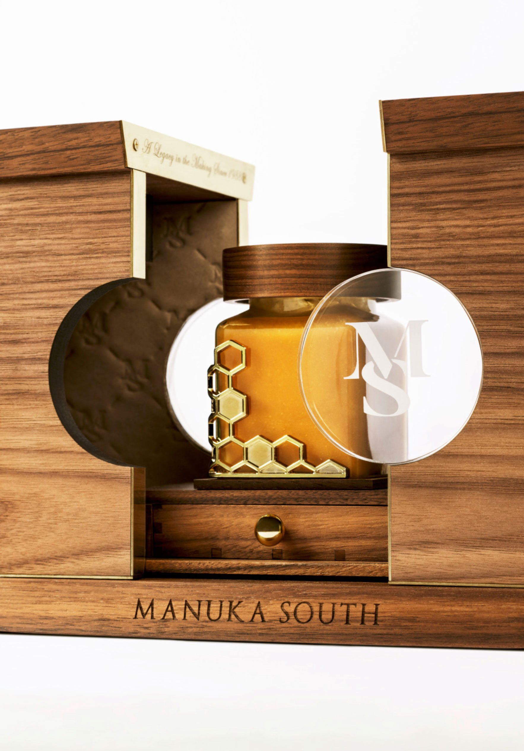 Premium product photograph of Manuka South honey packaging, showing the jar, wooden presentation case and luxury detailing.
