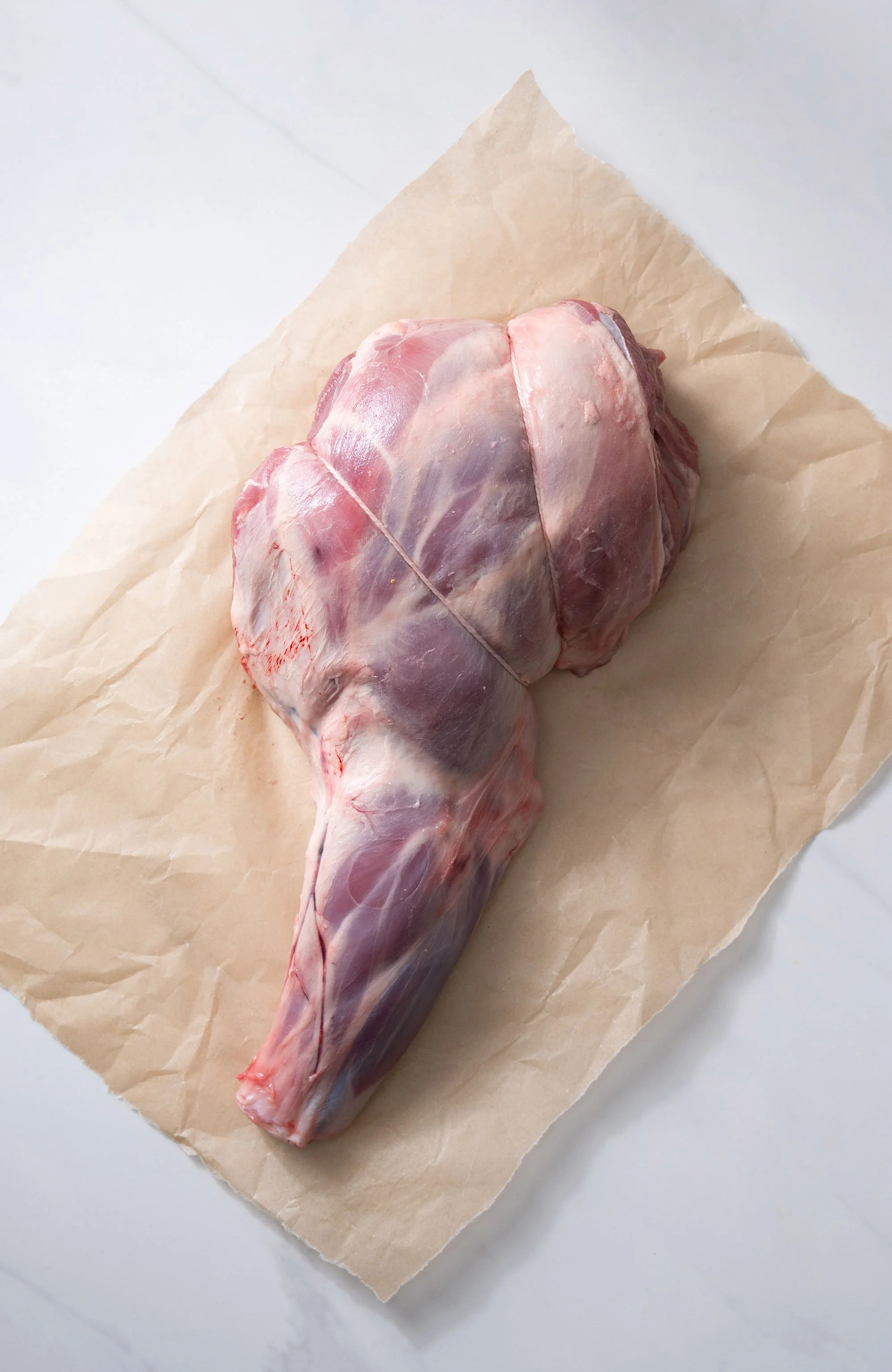 Raw leg of lamb wrapped in paper for a cookbook ingredient photograph.