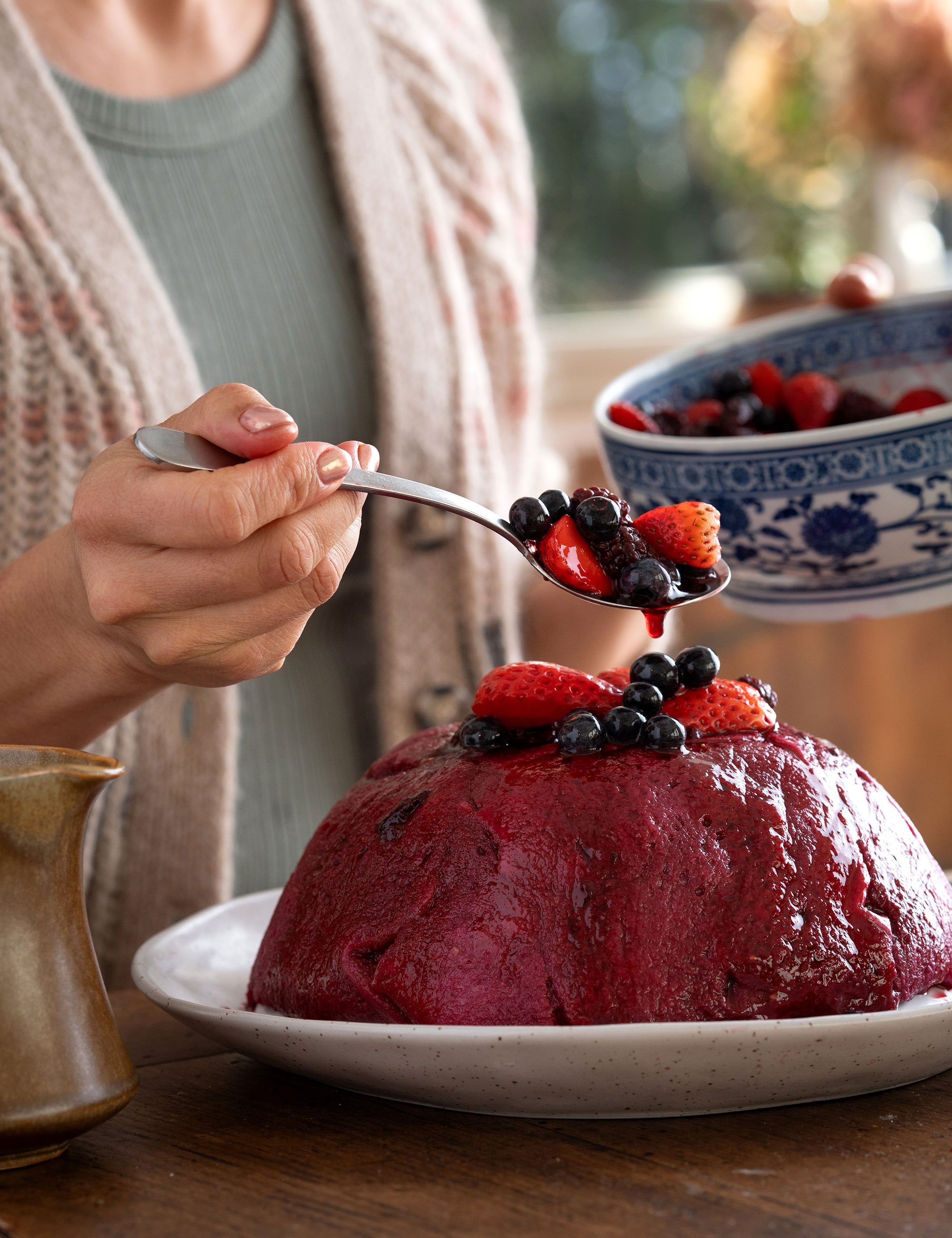 Spoon serving red berry dessert or compote onto a plated pudding outdoors.