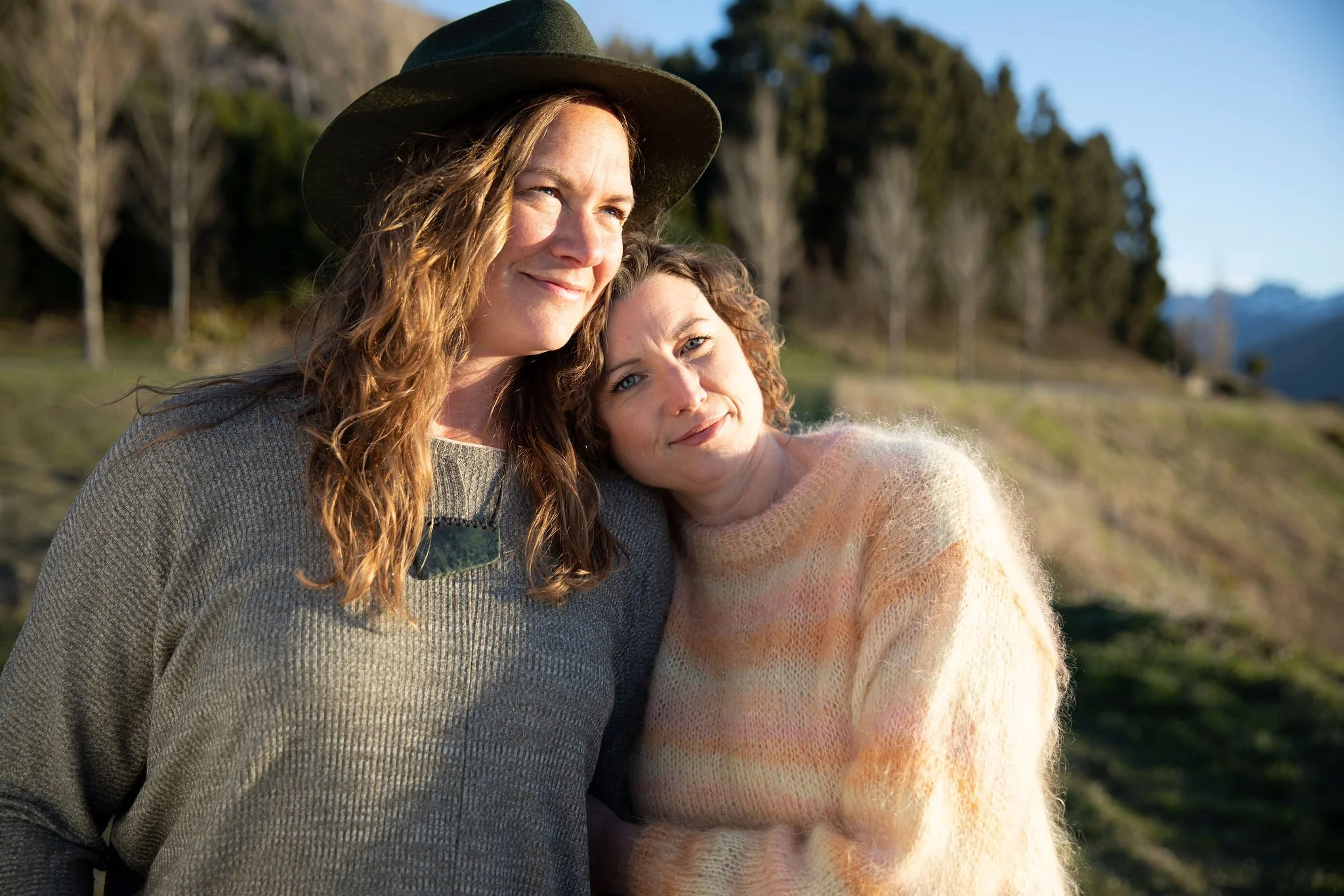 Two women embracing outdoors in warm natural light.