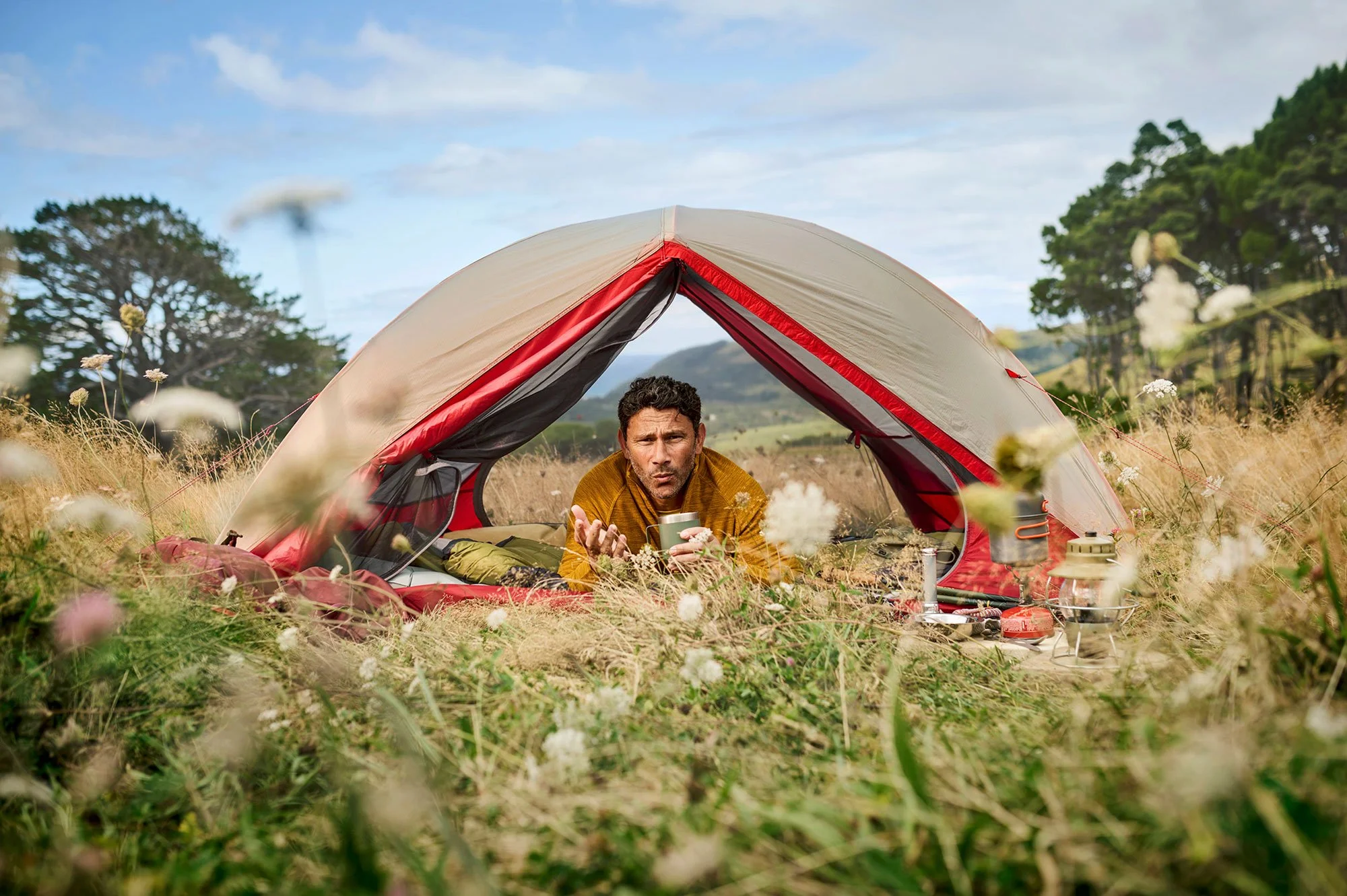 Camper smiling from inside a tent pitched in long grass.
