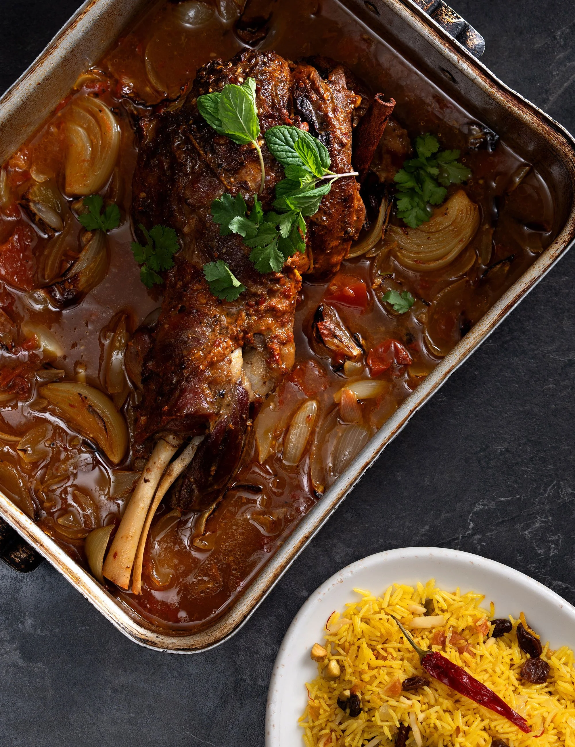 Roasted meat and vegetables in a tray with a side dish beside it.