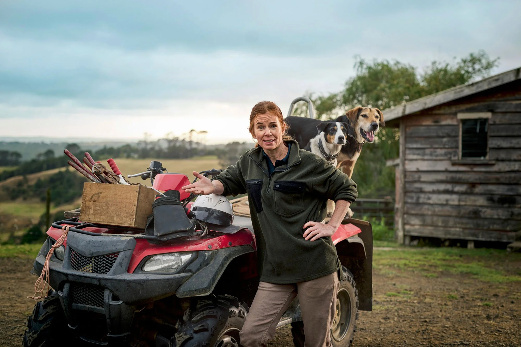 Farmer leaning on a quad bike with cattle and rural buildings behind him.