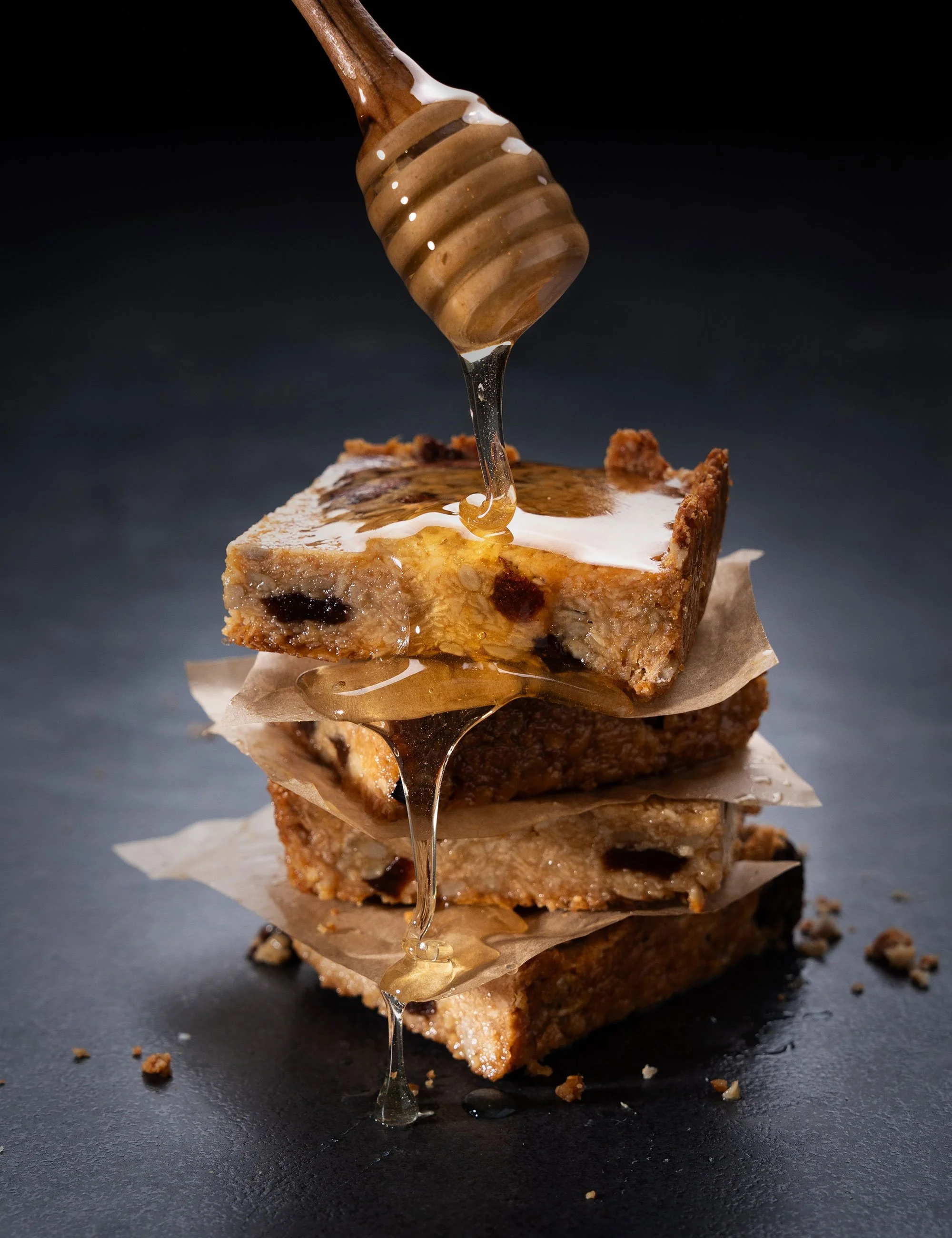 Honey being drizzled over stacked pastry or baklava on a dark studio background.