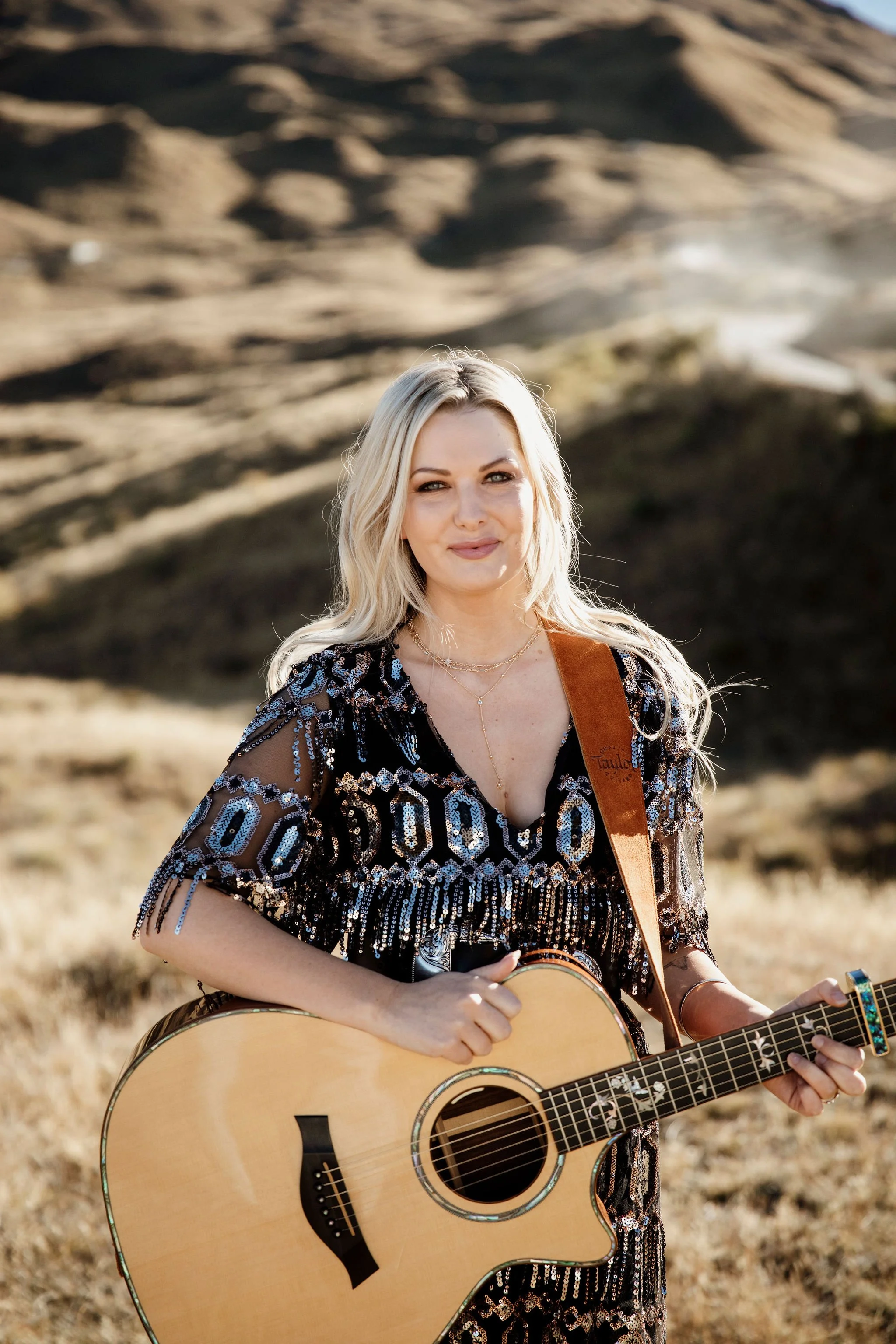 Musician Miranda standing with an acoustic guitar against a rocky outdoor backdrop.