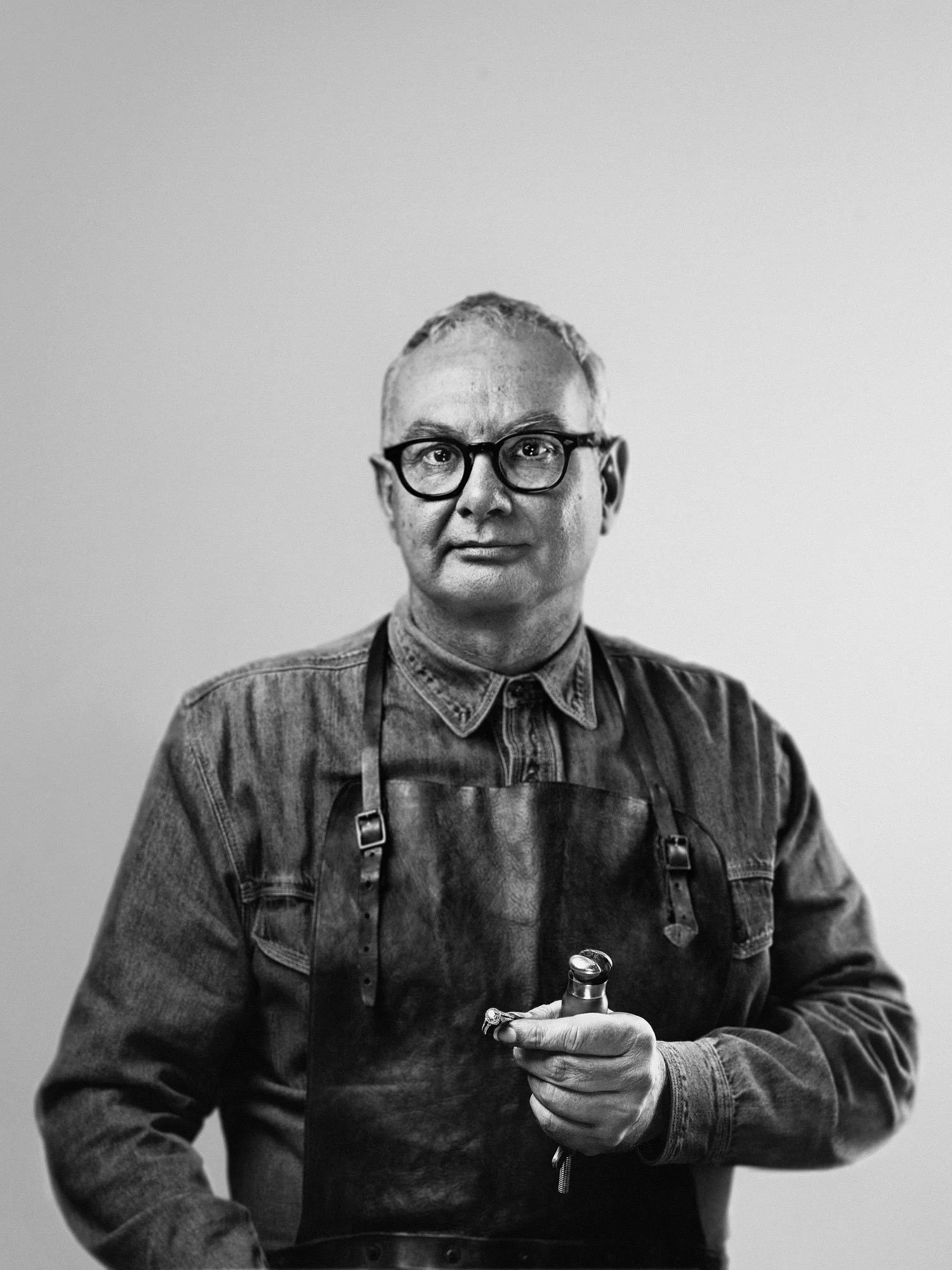 Black-and-white portrait of an older artist holding a cup in a studio setting.