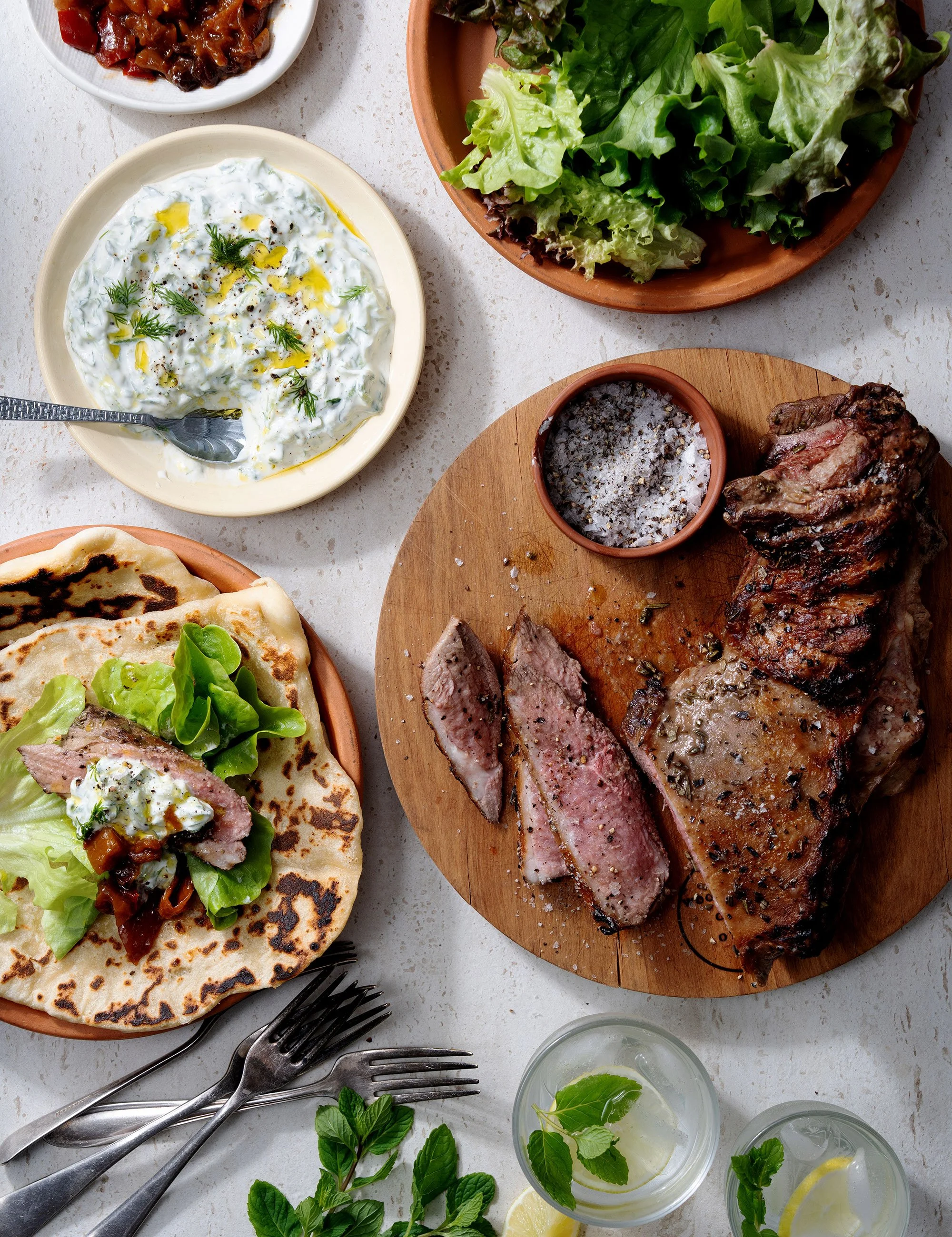 Overhead restaurant spread with grilled steak, salads and shared plates.
