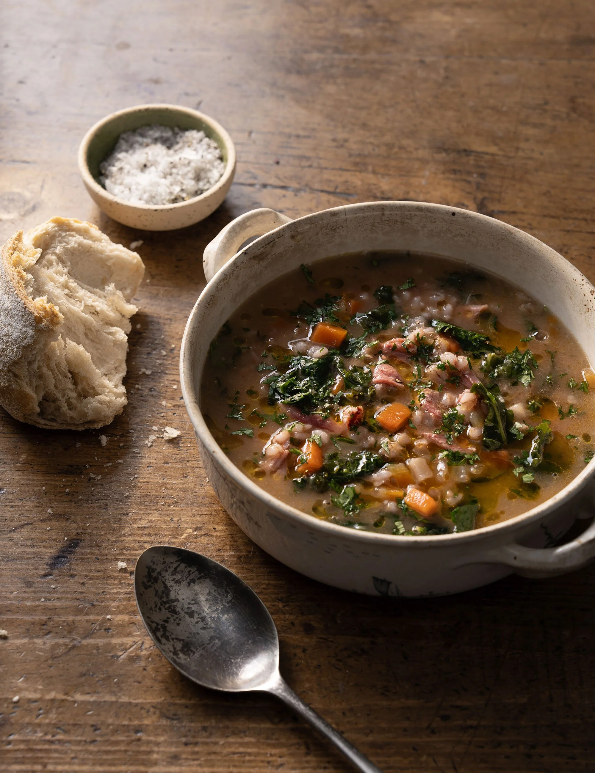 Bowl of hearty soup with beans and greens on a rustic wooden table.