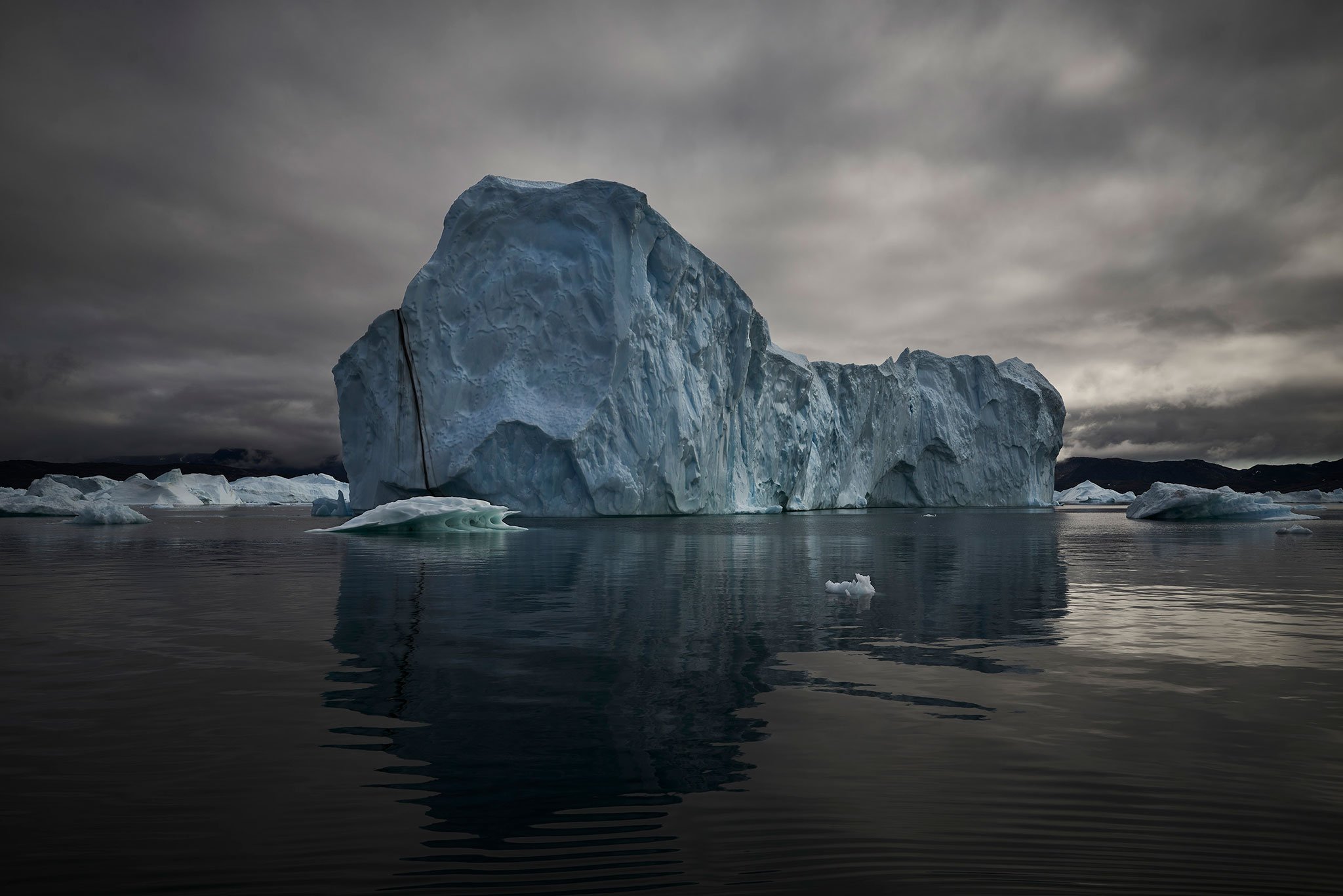 Dramatic fine art landscape photograph of a weathered iceberg against brooding cloud, emphasizing scale, texture and atmosphere.