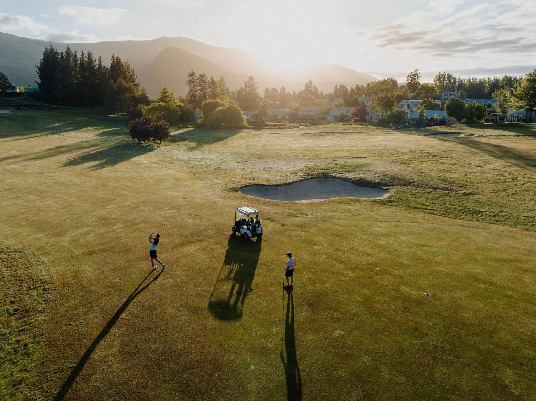 Aerial view of golfers and carts on a Millbrook Resort fairway in warm afternoon light.