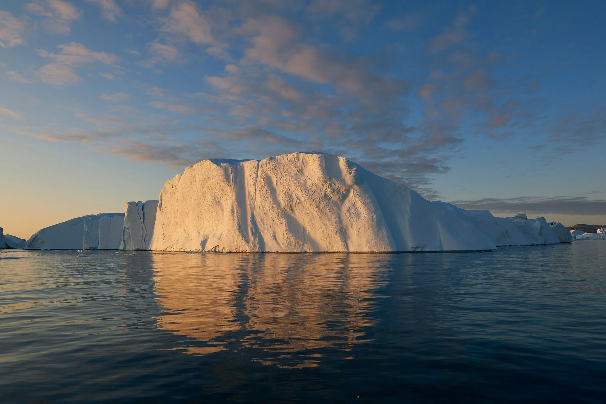 Atmospheric iceberg landscape with soft dawn light, icy detail and mirror-like reflections across a tranquil Arctic seascape.