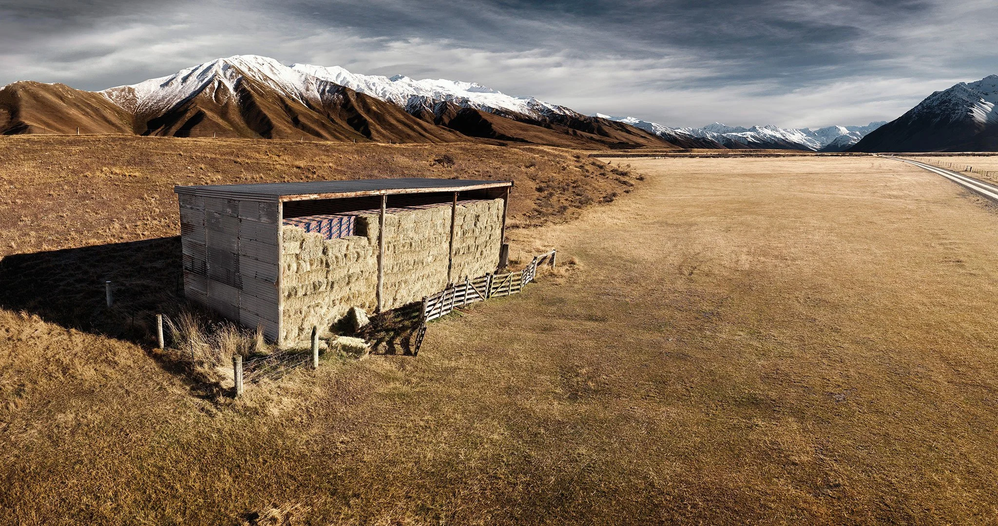 Expansive landscape photograph of a hay shed in open country, using scale, light and space to create a quiet conceptual feel.