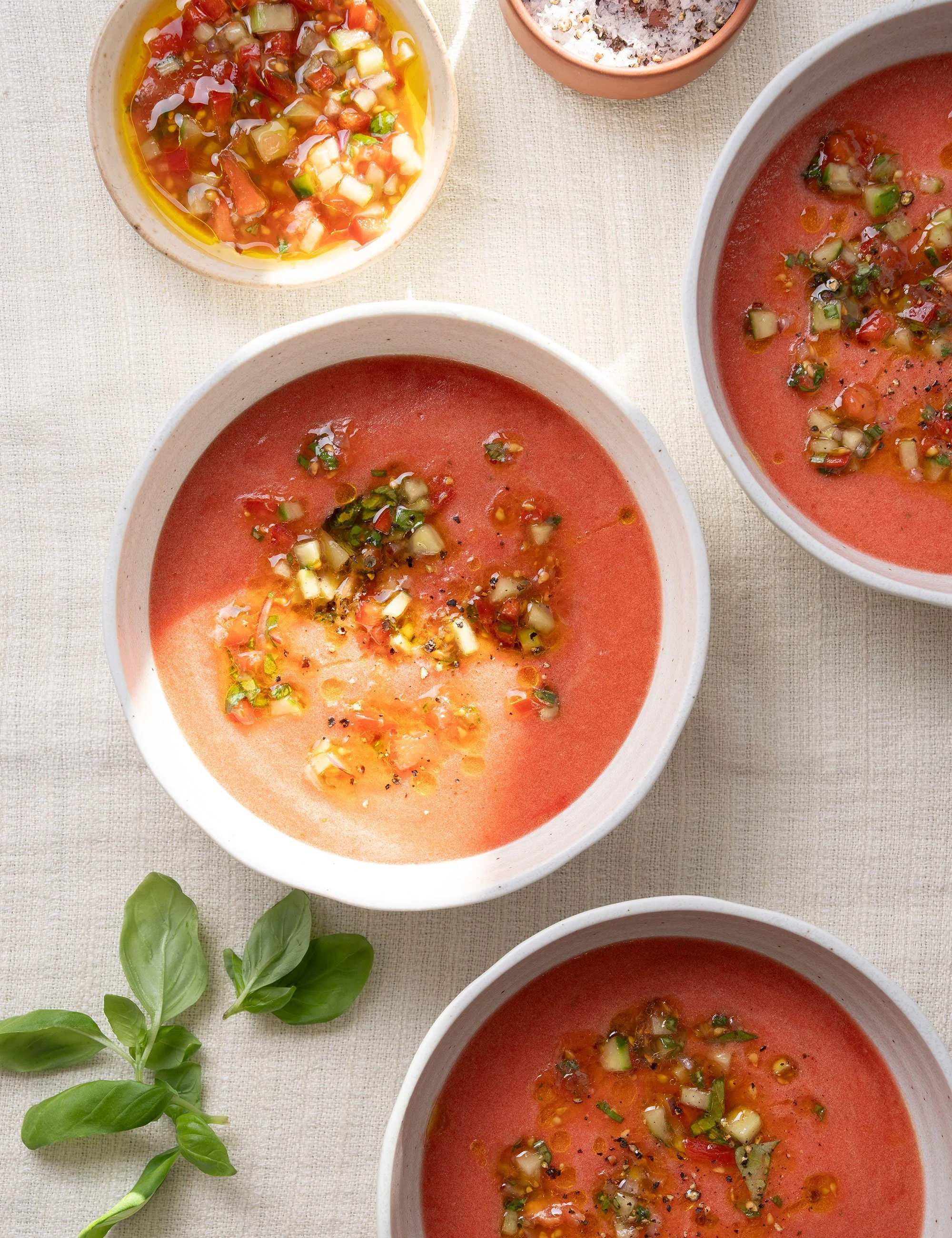 Overhead food photograph of bowls of soup with garnishes on a light table.