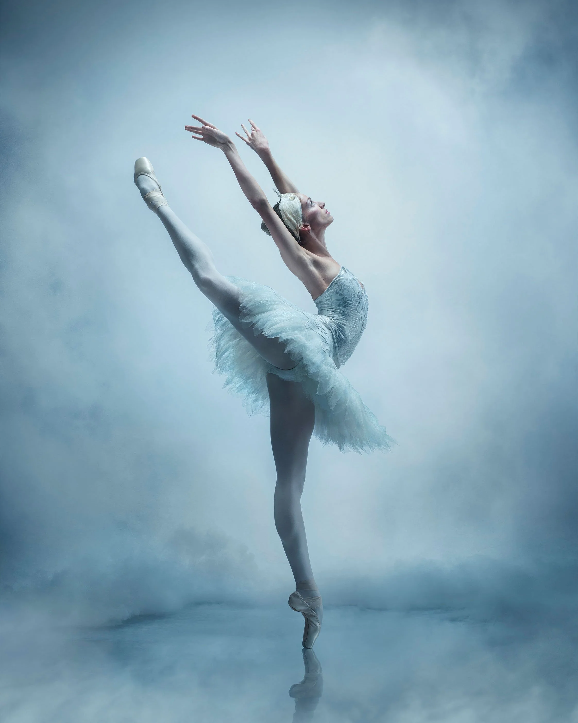 Ballet dancer extended en pointe in a cloud of powder against a blue studio backdrop.