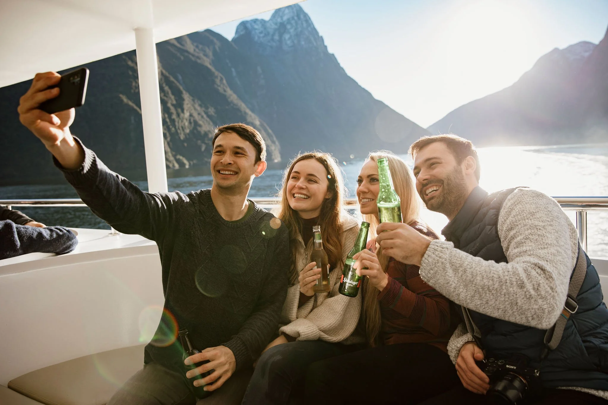 Friends taking a selfie and holding drinks on a scenic boat cruise through Milford Sound.