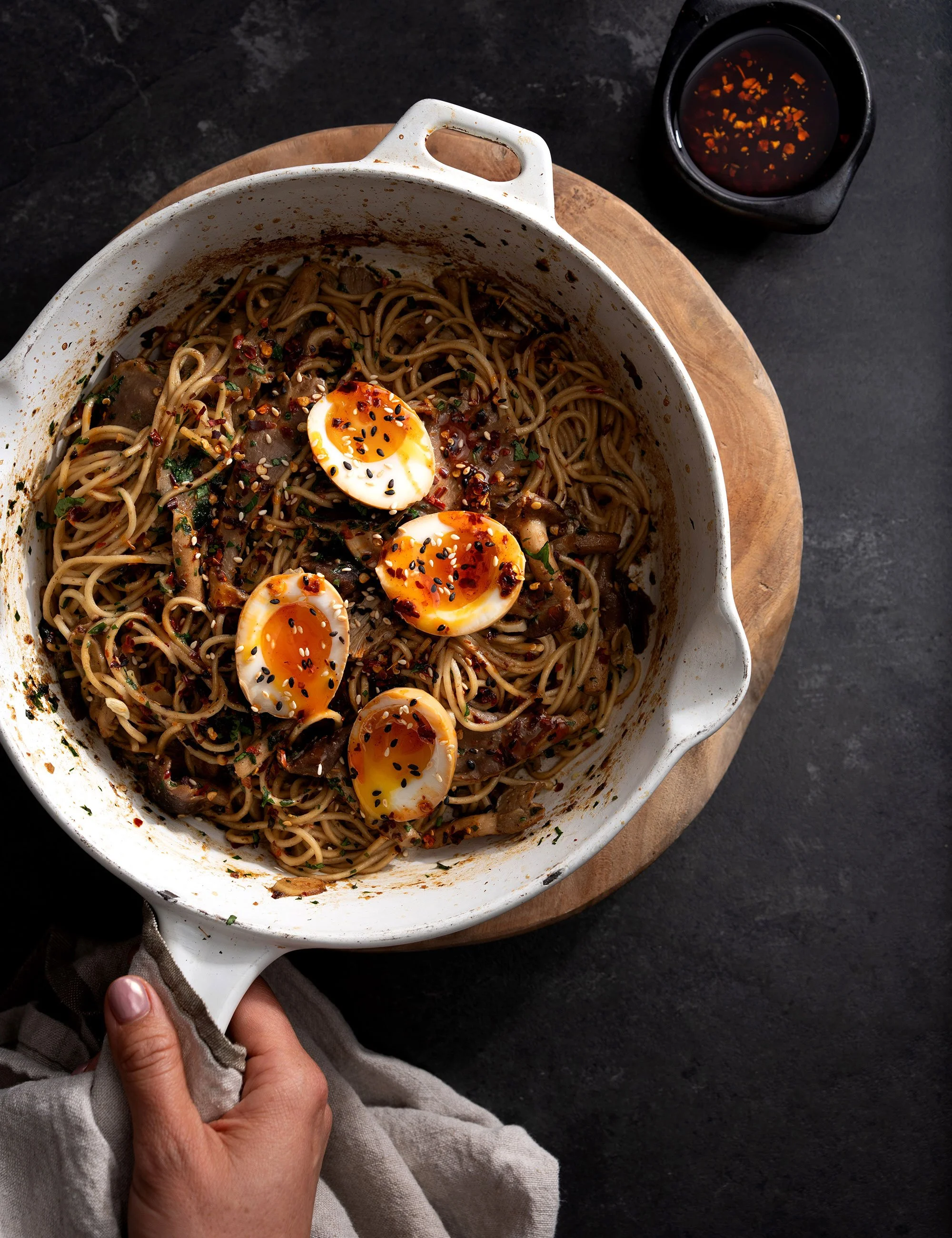 Pot of dark noodle or grain dish topped with halved eggs in an overhead food photograph.