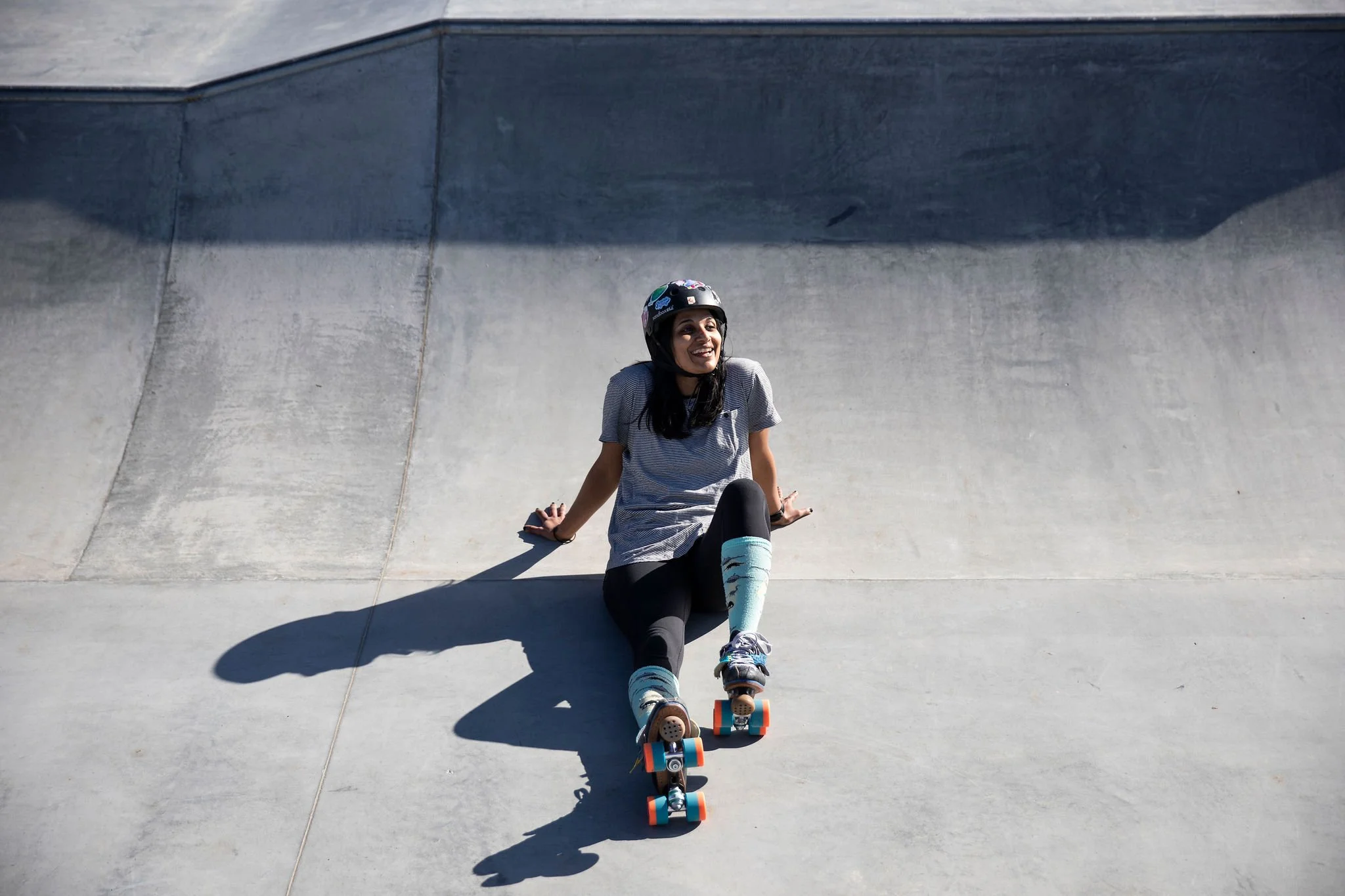 Skateboarder standing in a concrete bowl with a long shadow in bright sun.