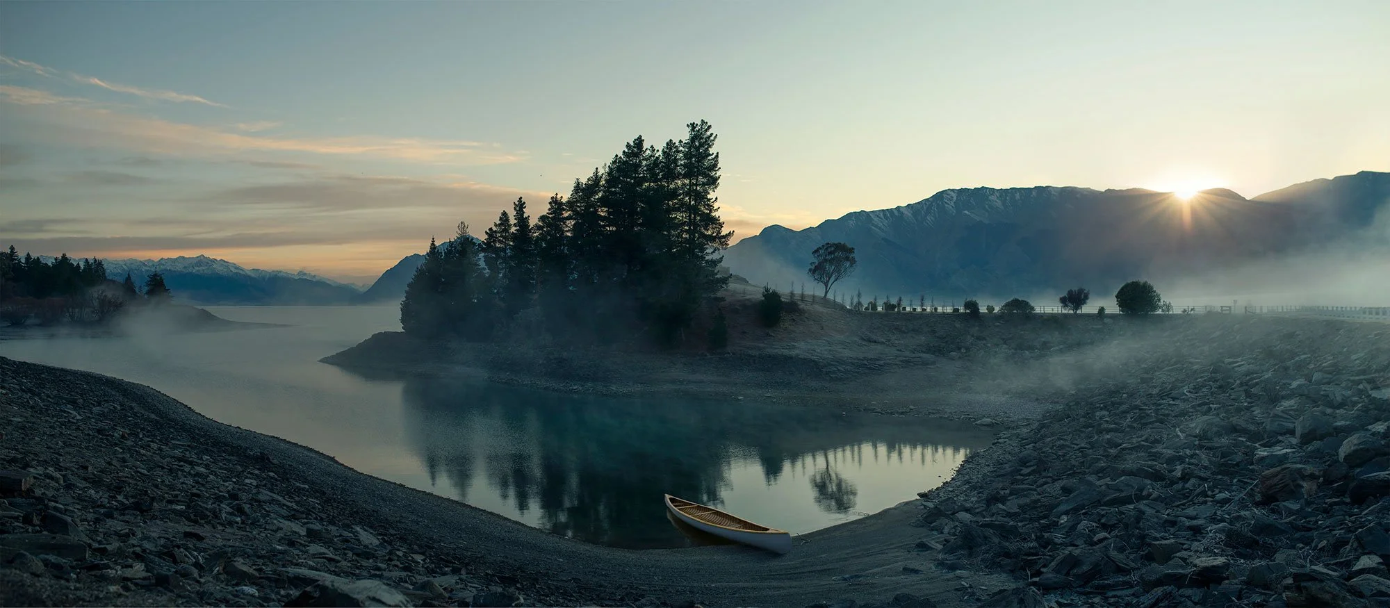 Panoramic Lake Hawea shoreline with mist, still water and mountains at sunrise.