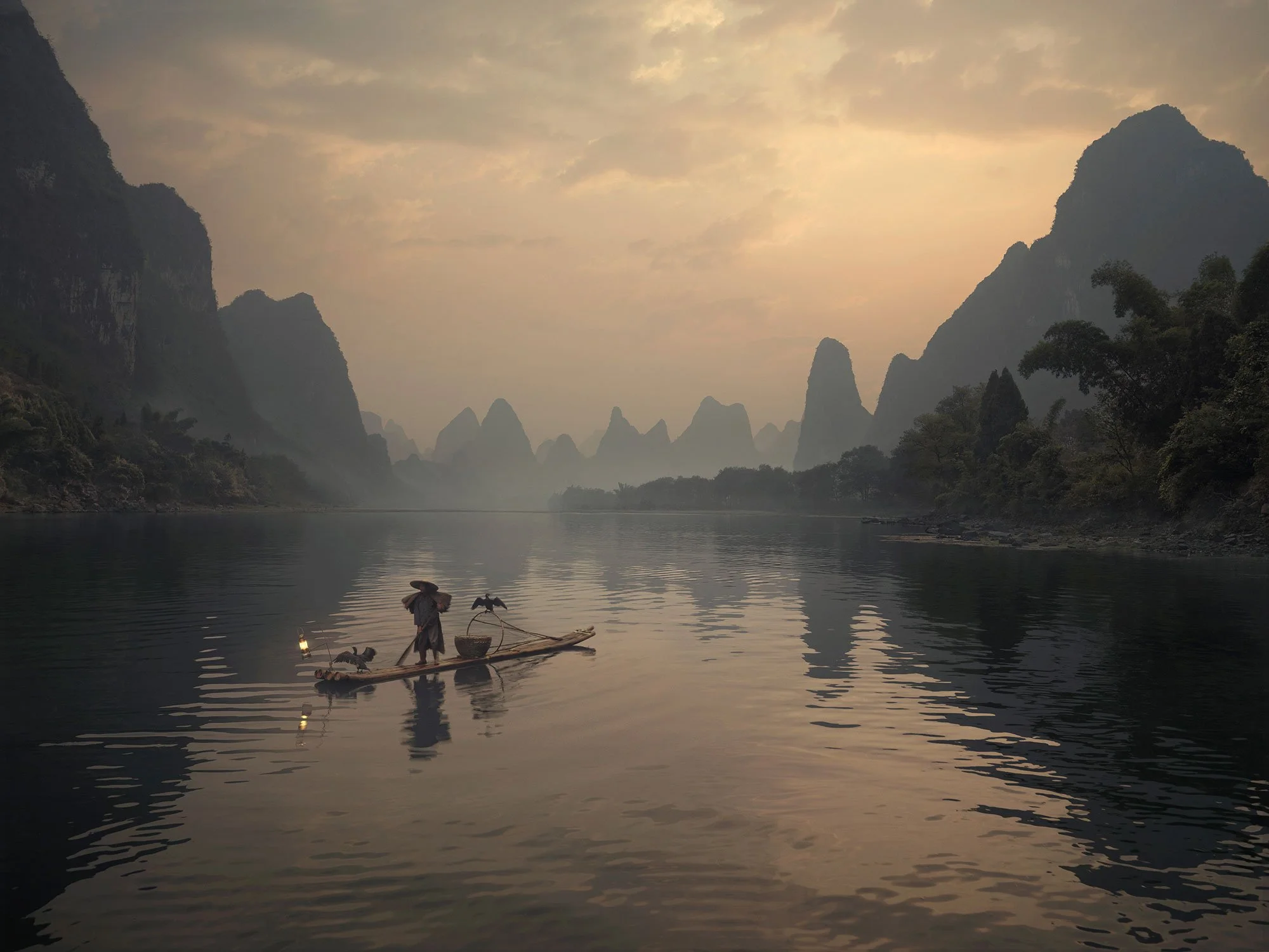 Atmospheric travel landscape photograph of a lone fisherman on still water, framed by layered mountains and fading evening light.