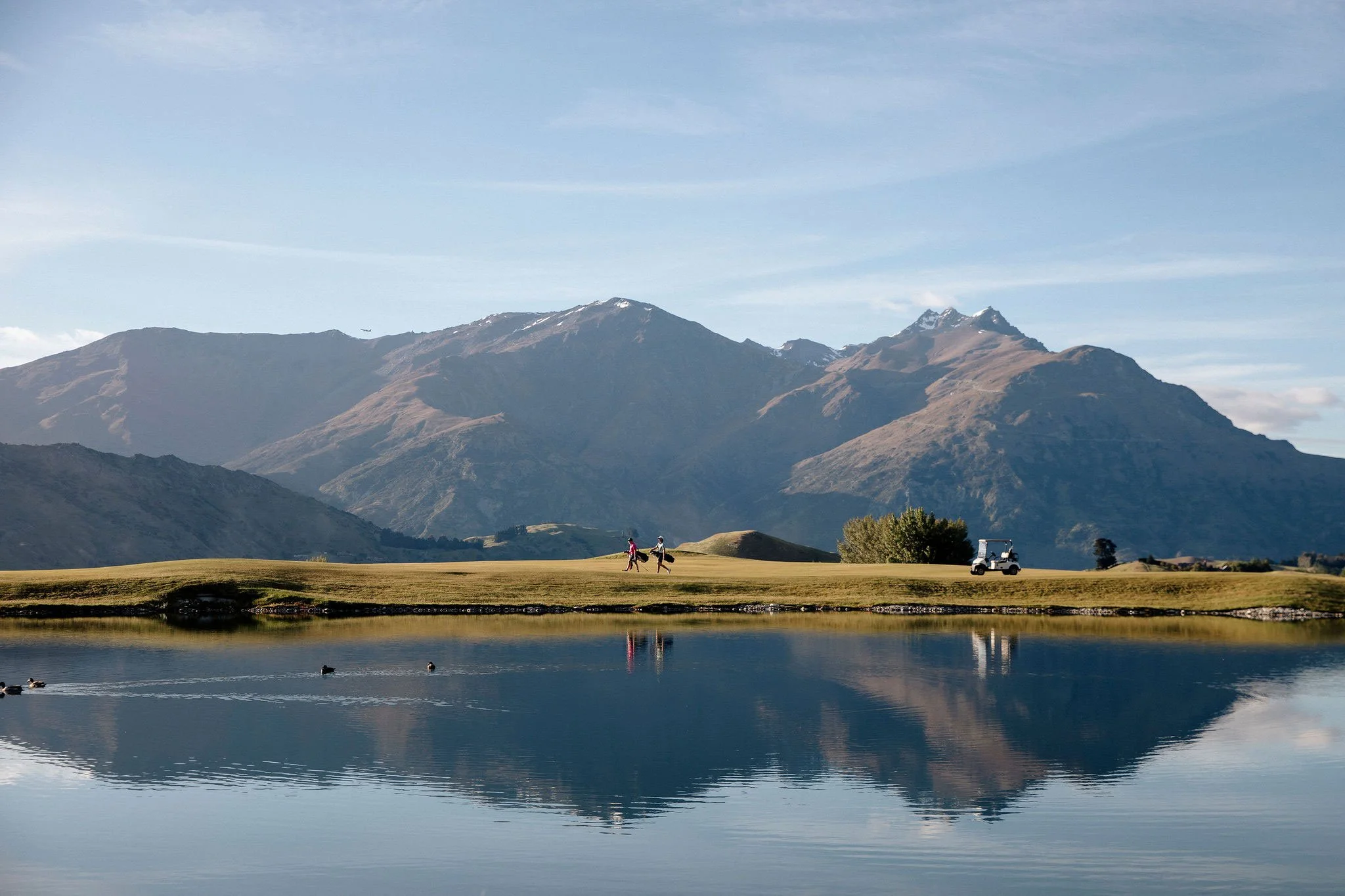 Golfers on a lakeside fairway with mountain reflections at Millbrook Resort in Queenstown.