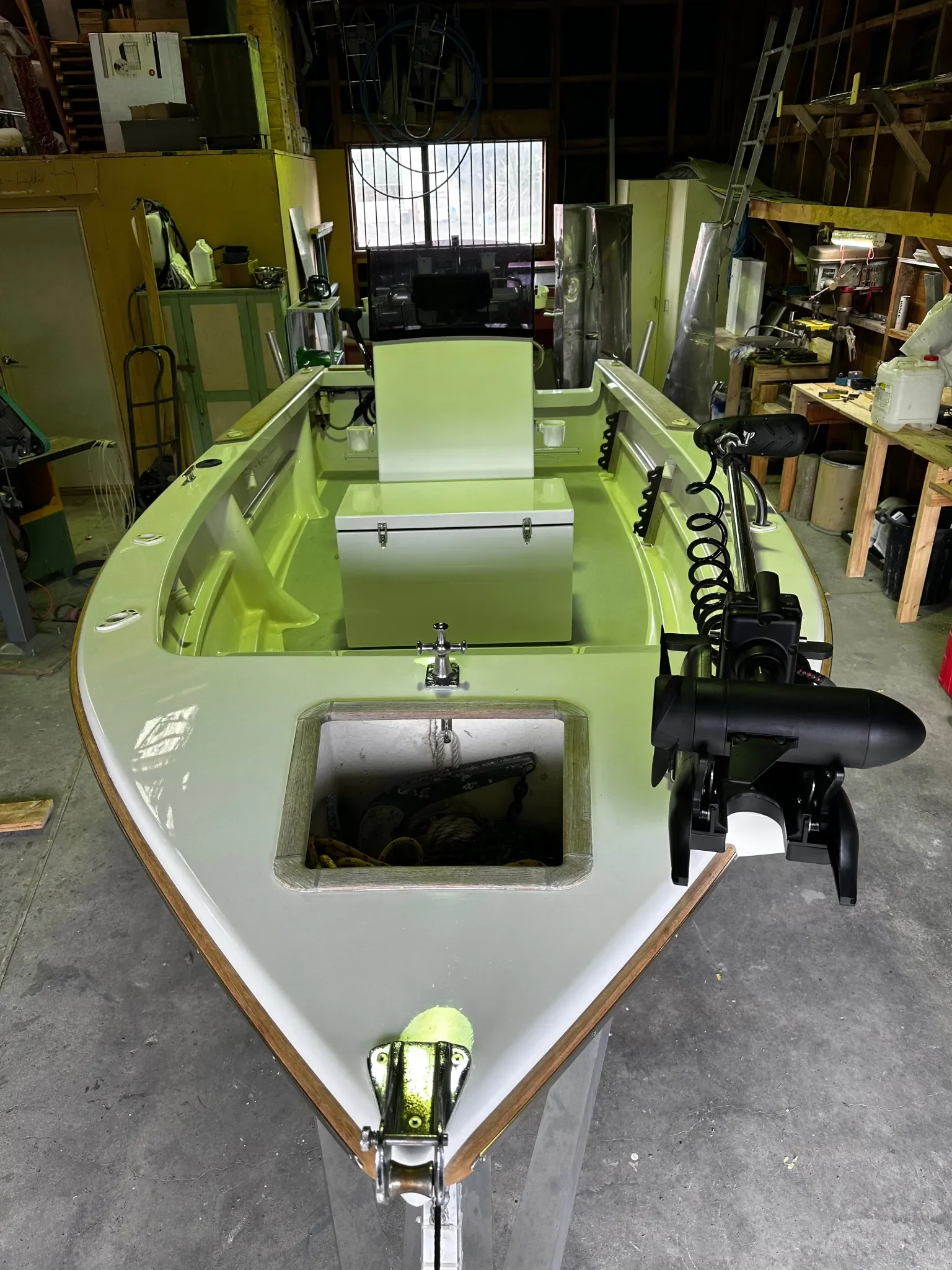 A boat hull inside a workshop with tools and equipment around it, showing an opening in the front and a mount at the bottom. There is a steering system and a black motor attached at the back.