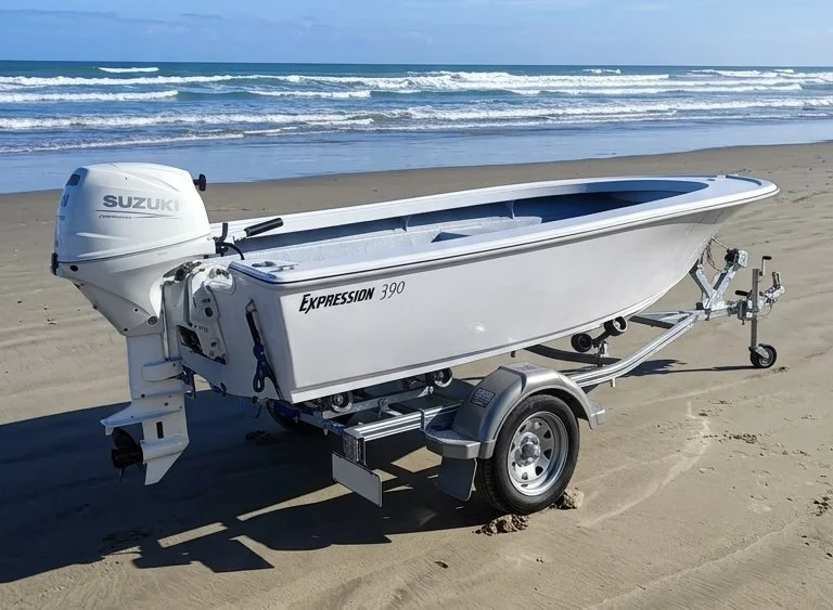 Small white motorboat on a trailer parked on sandy beach with ocean waves in the background.