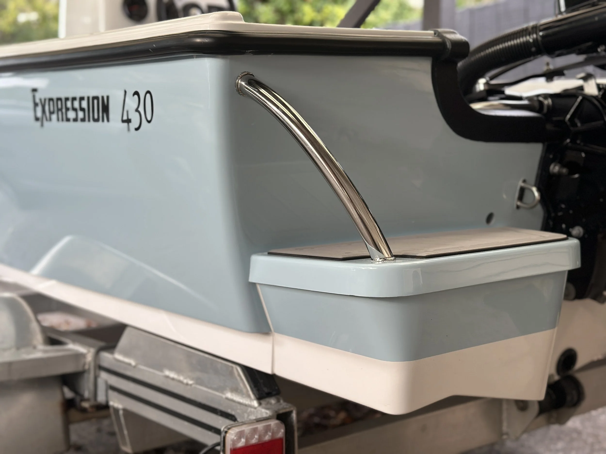 A close-up view of a Food truck with the sign 'EXPRESSON 430' on the side, with a metal tube protruding from the side, and a part of the truck's wheel and bumper visible. In the background, there is a blurred view of trees and a structure.