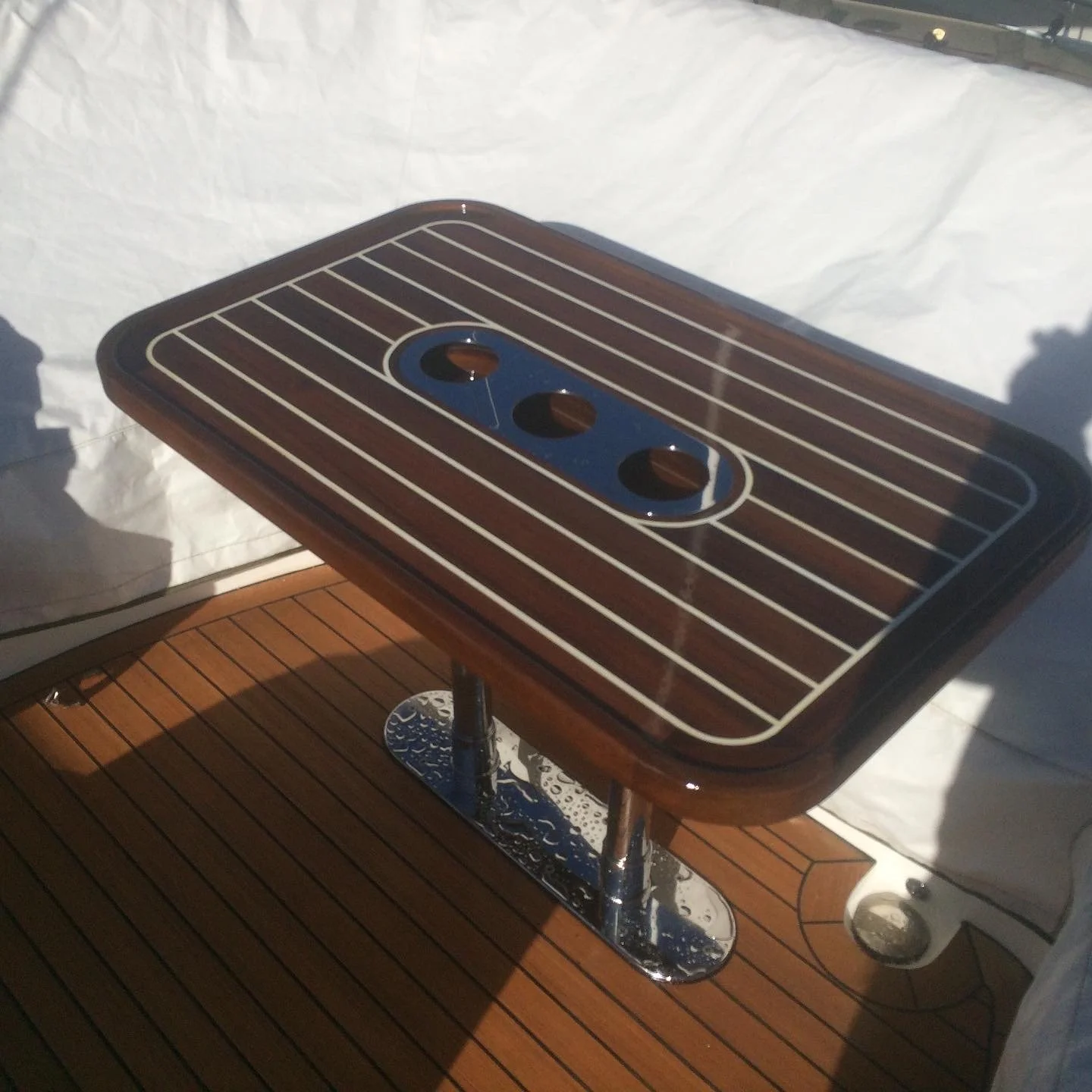 A rectangular wooden table with a striped pattern on the surface, featuring three circular openings and a central oval-shaped black section, supported by a metal pedestal base.