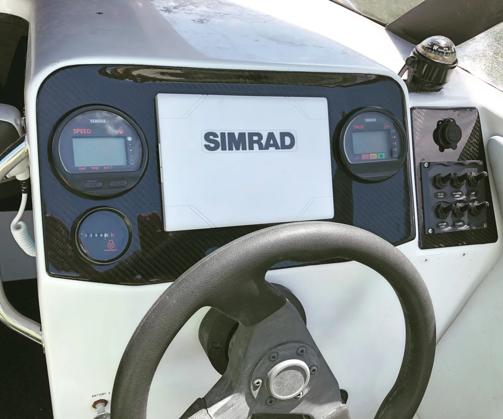 Close-up view of a control panel on a Yamaha boat with a SIMRAD navigation system, speed and tachometer gauges, and a compass mounted on the top right corner.