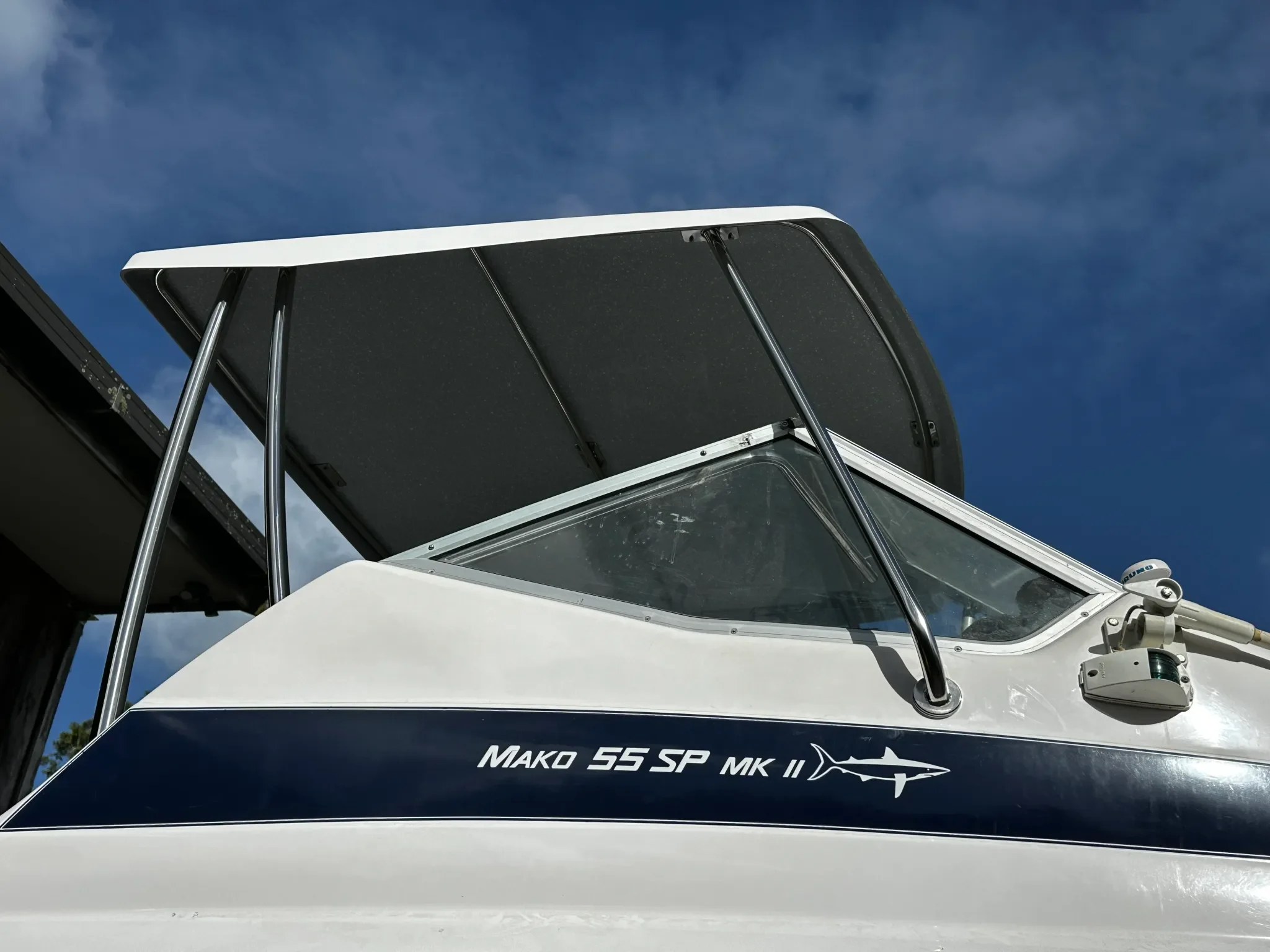 Close-up view of a boat’s T-top roof with a clear blue sky in the background. The boat's name, "MAKO 55 SP MK II," is visible on the side, along with a shark logo.