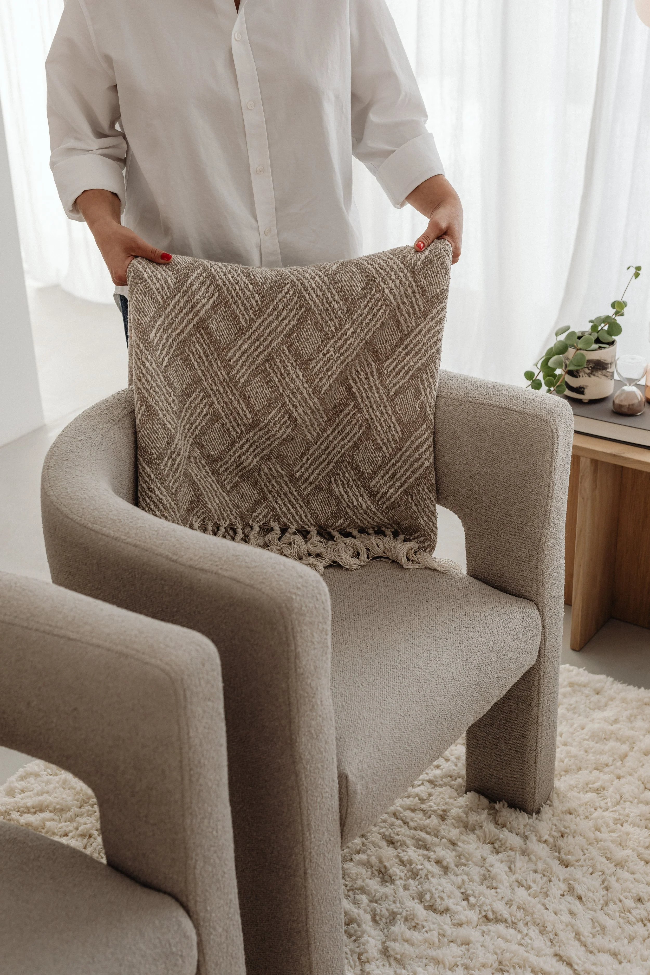 Cleaner adjusting a beige patterned pillow on a light-colored armchair in a cozy, well-lit room with a cream shag rug in a beautiful Gold Coast home.