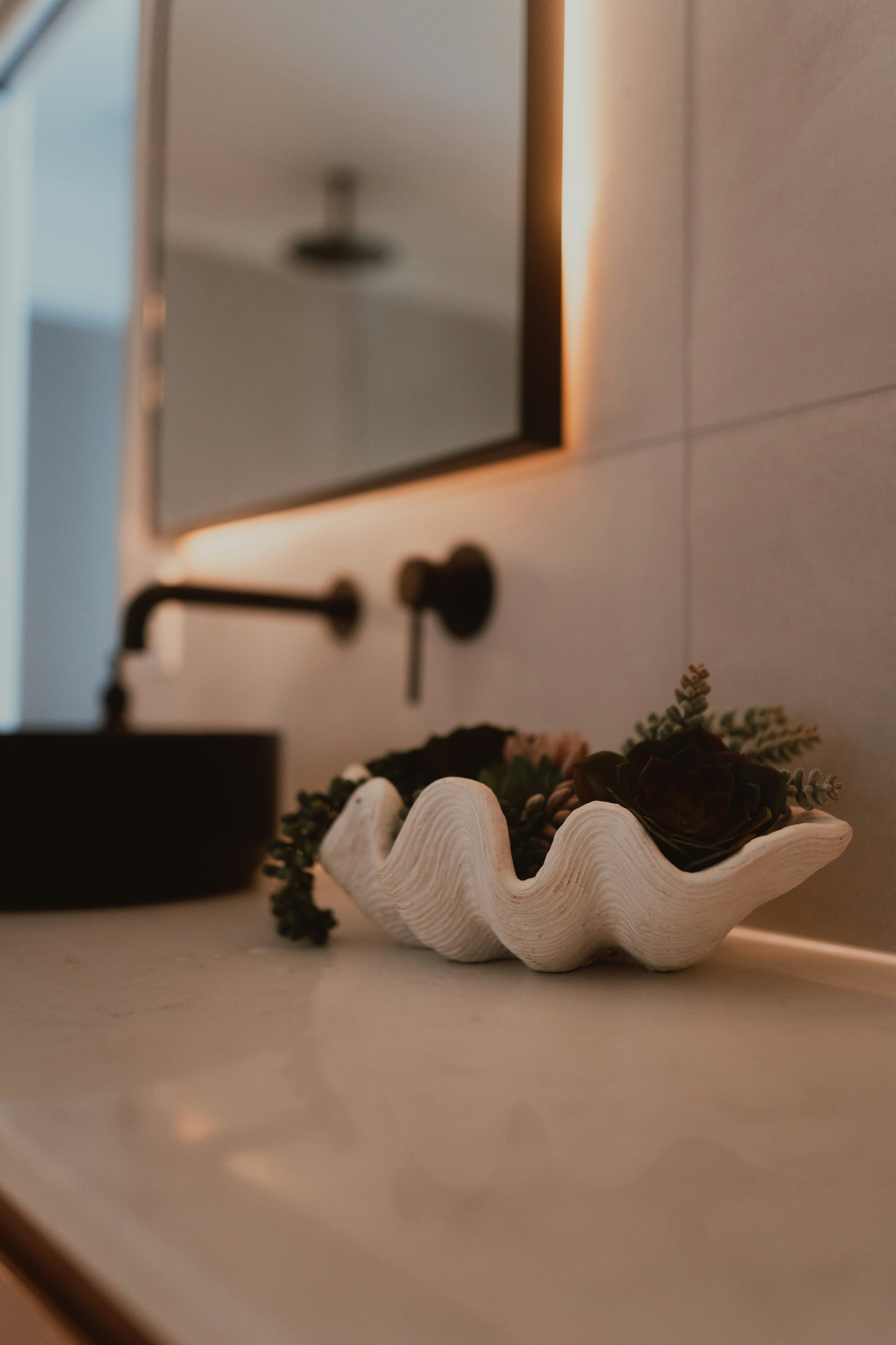 A decorative white ceramic dish shaped like a scalloped shell with green foliage and a small dark brown object inside, placed on a light-colored surface.