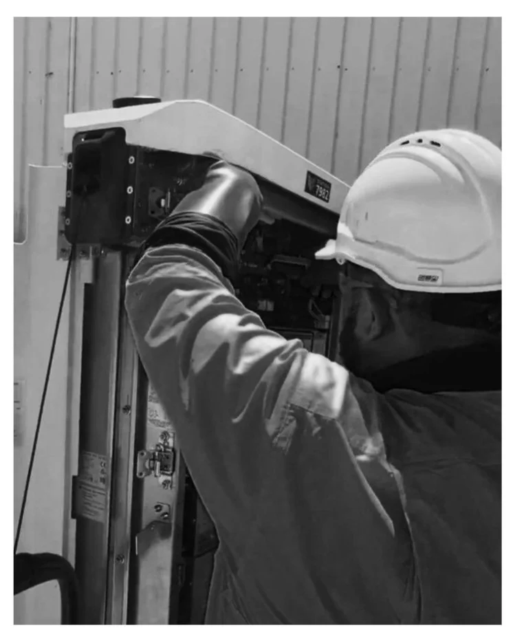 A worker in a hard hat is repairing or installing electrical equipment inside an industrial panel or control box.
